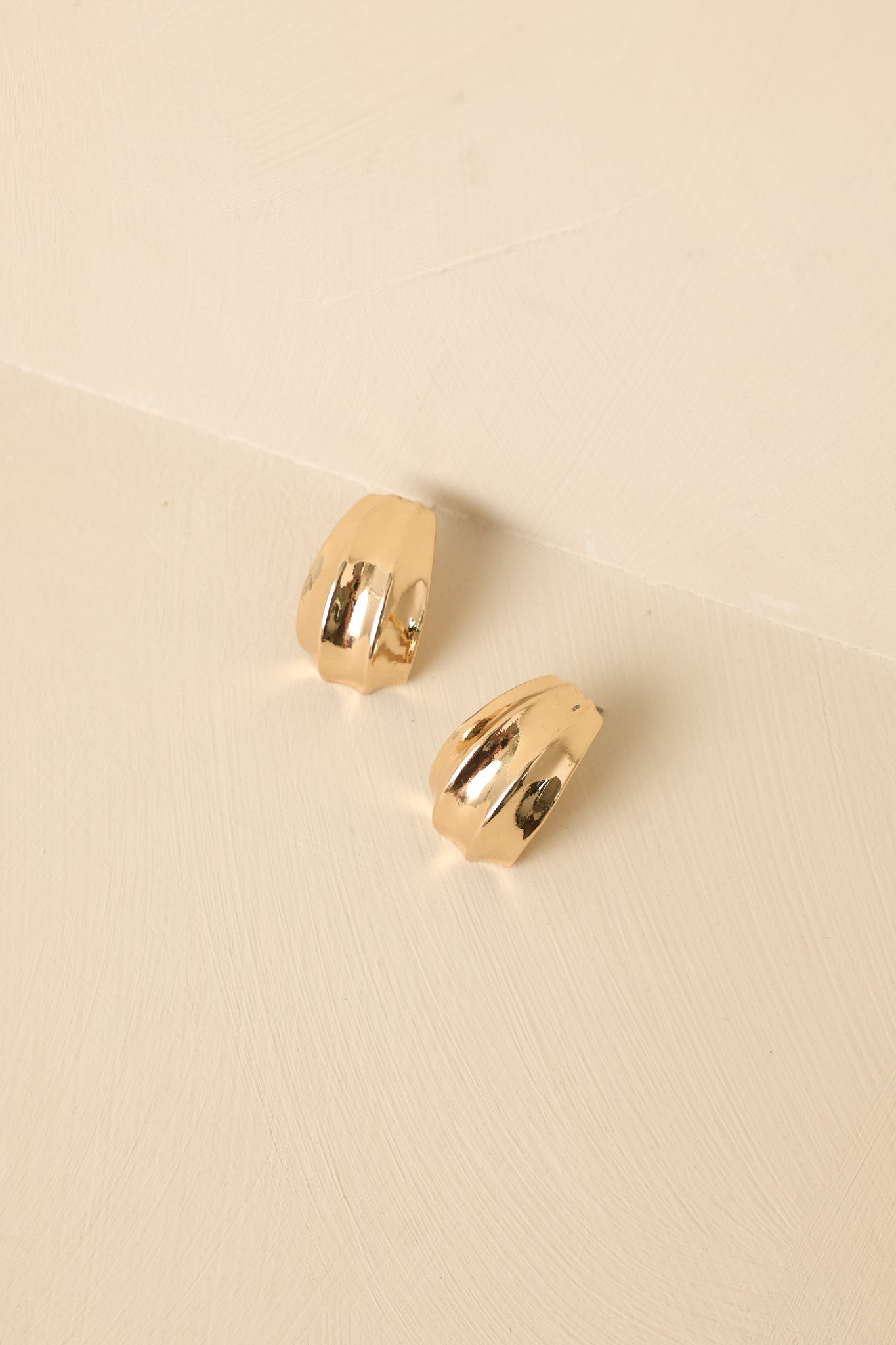Tight crop emphasizing the polished gold-tone surface and accordion-inspired design of the earrings.