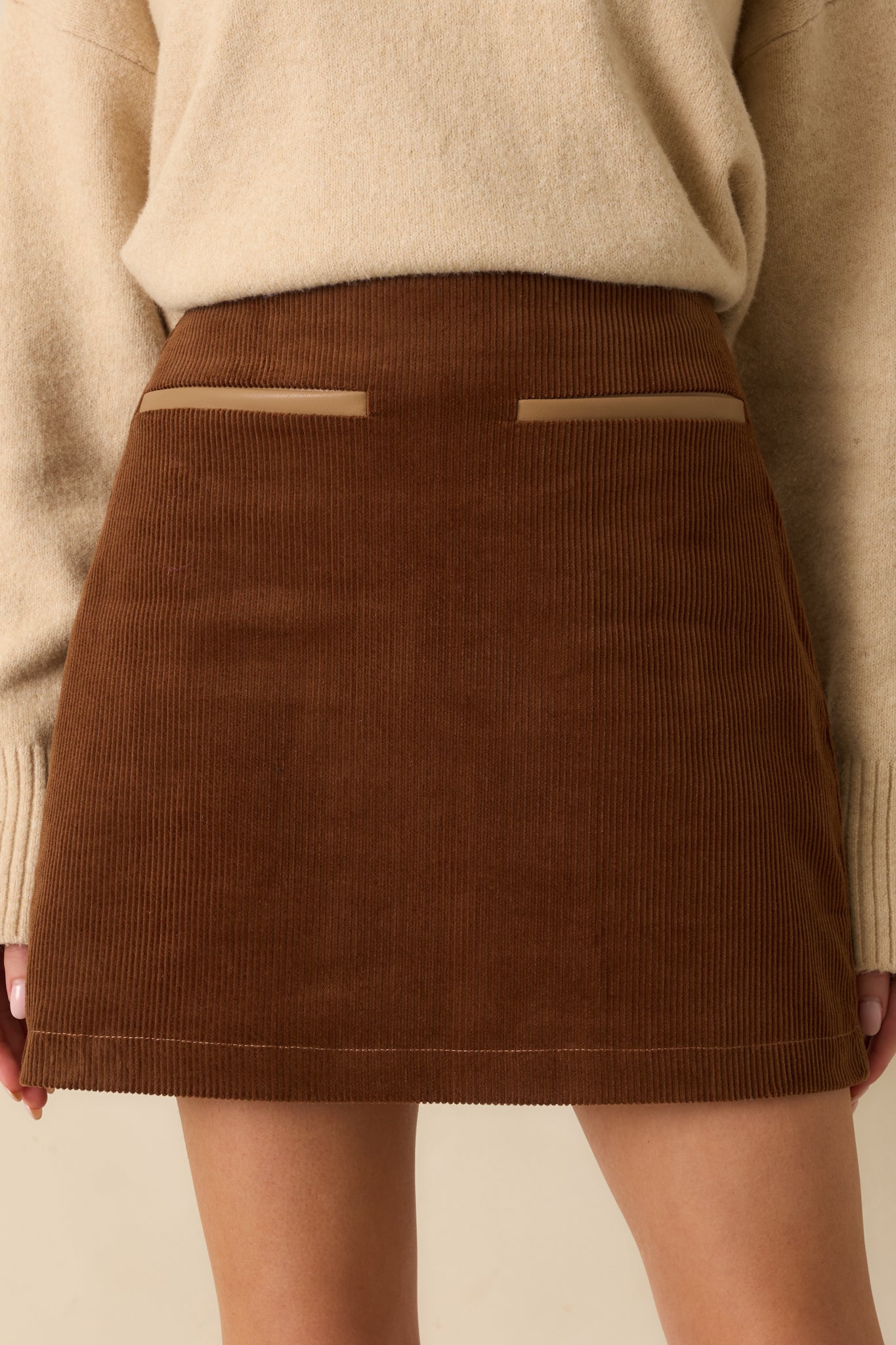 Tight shot of cinnamon brown corduroy fabric showing texture and contrast trim on faux pockets.
