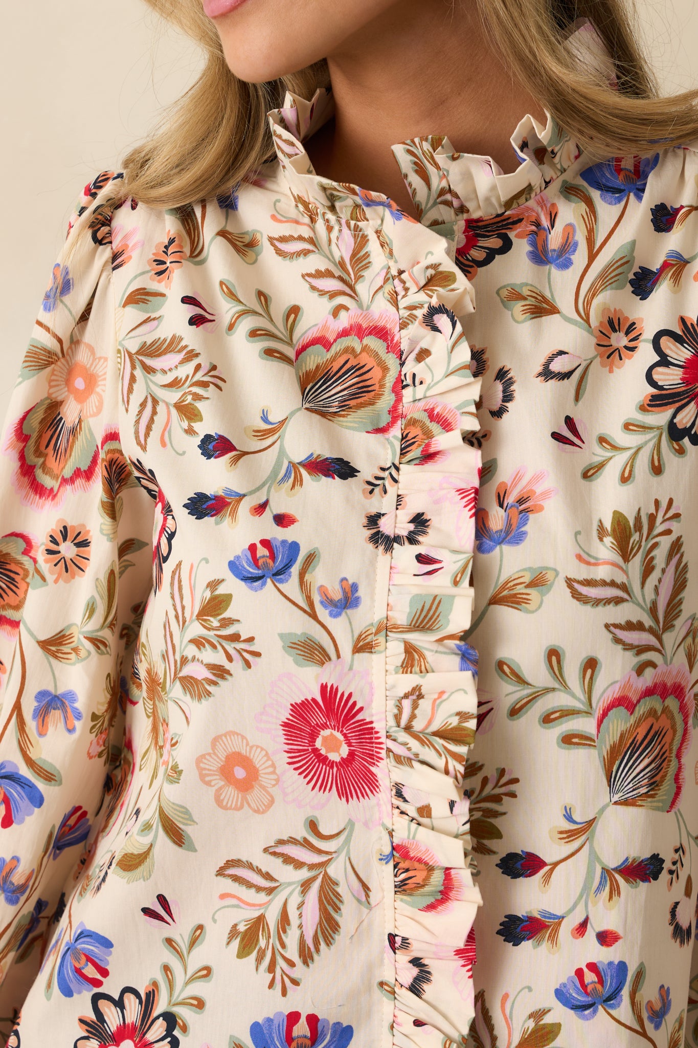 Tight shot of ivory top fabric showing floral print, button detailing, and ruffled edges.