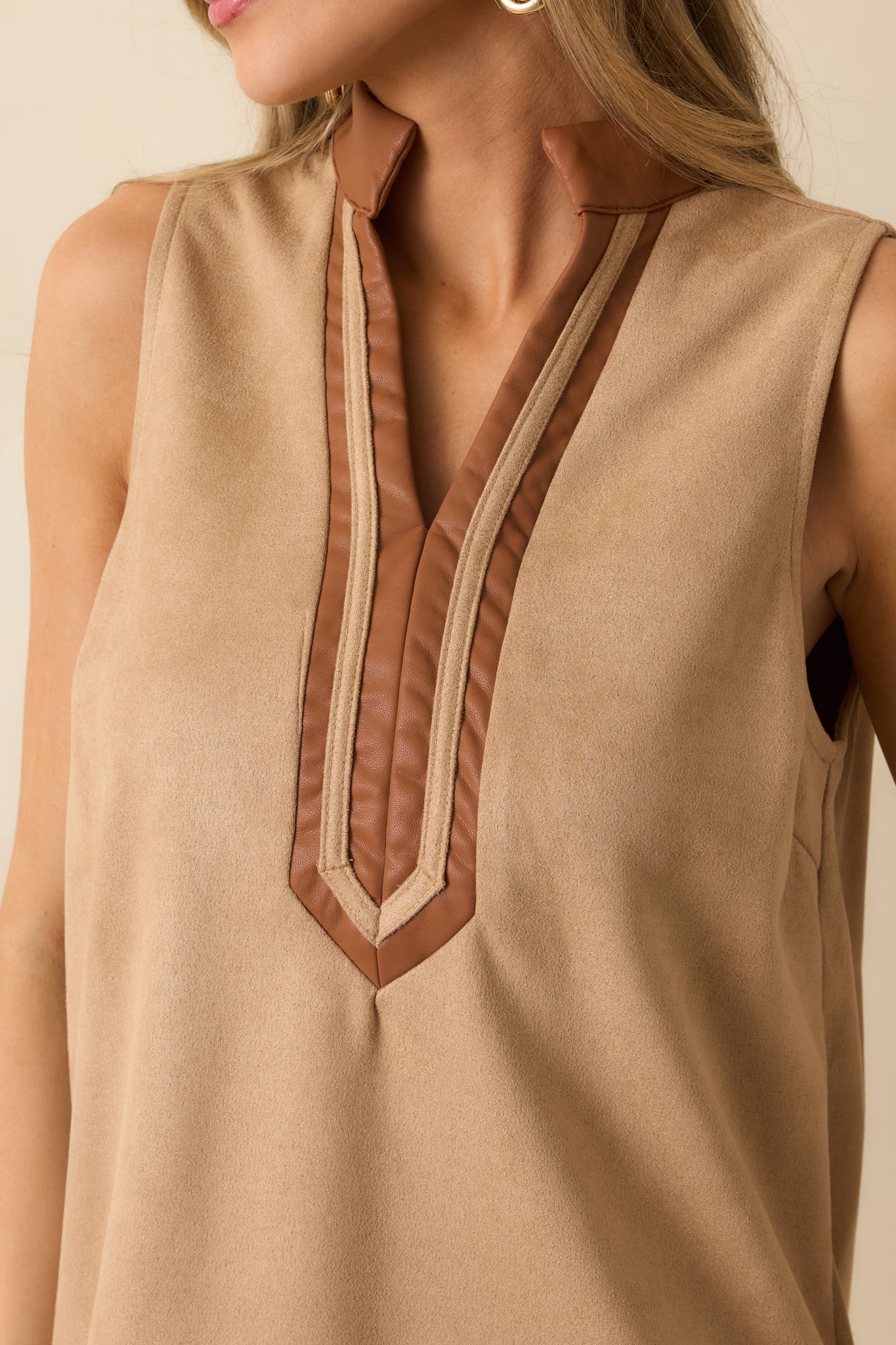 Tight shot of tan faux suede fabric with contrasting faux leather trim on neckline and hem.
