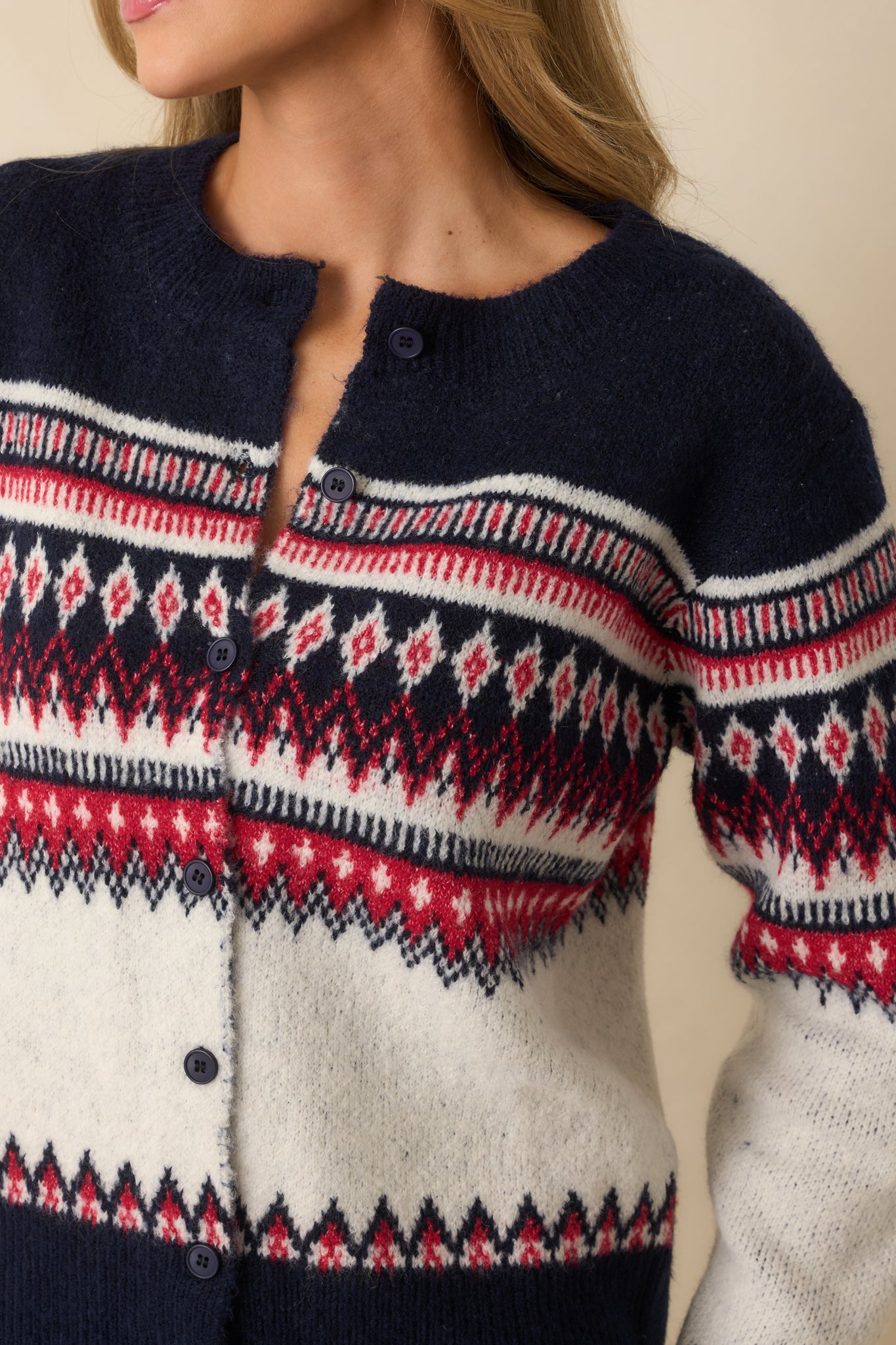 Tight view of navy and red Fair Isle pattern, buttons, and textured knit fabric of the cardigan.