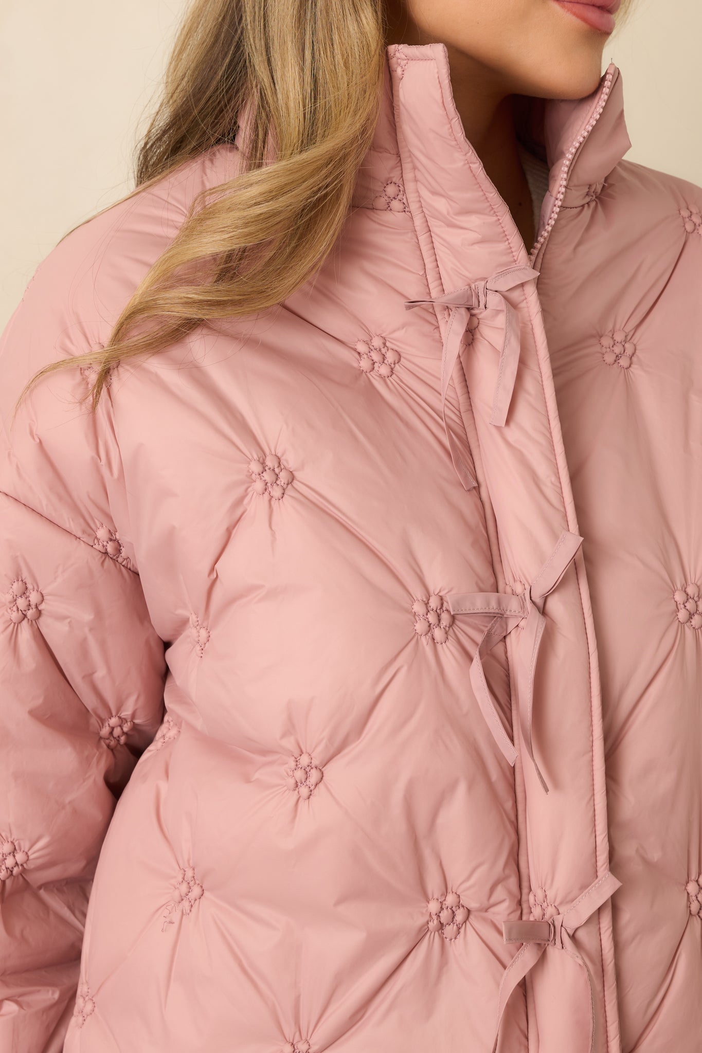 Tight view of the blush pink quilted fabric showcasing floral-inspired stitching and fine tie accents along the front.