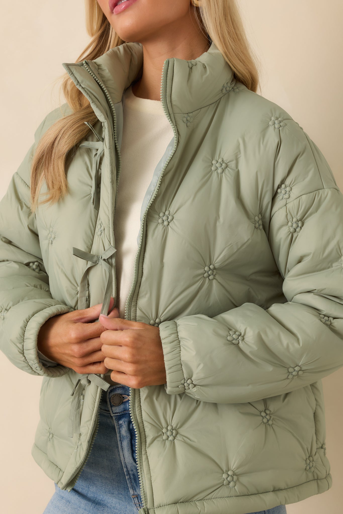 Tight view of the sage green quilted fabric showcasing the floral-inspired stitching and delicate tie accents along the front.