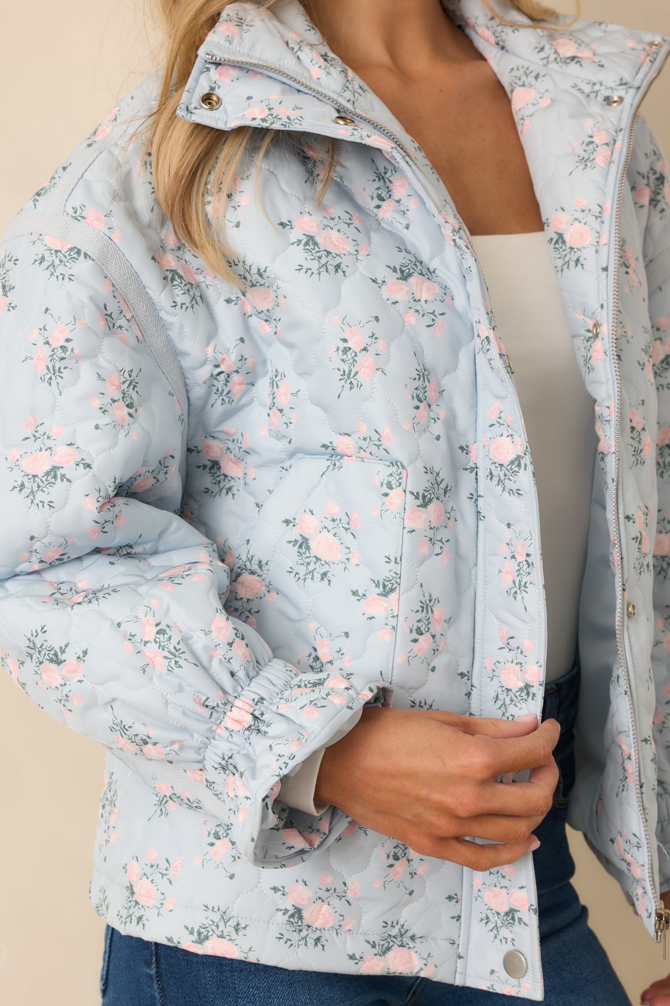 Tight view of the light blue quilted jacket fabric showcasing pink floral motifs, green foliage accents, and stitched texture.