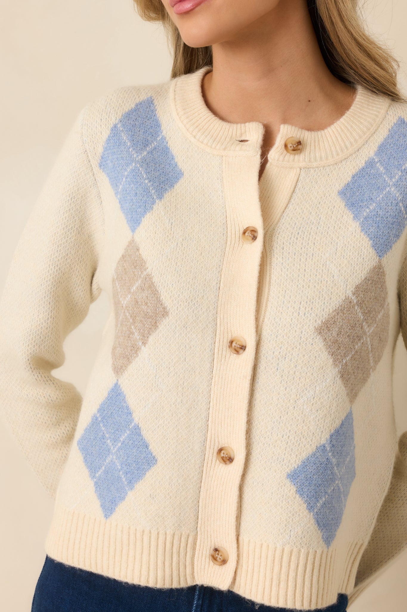 Tight view of the cardigan fabric showing soft argyle stitching in blue and taupe with ribbed trim accents.