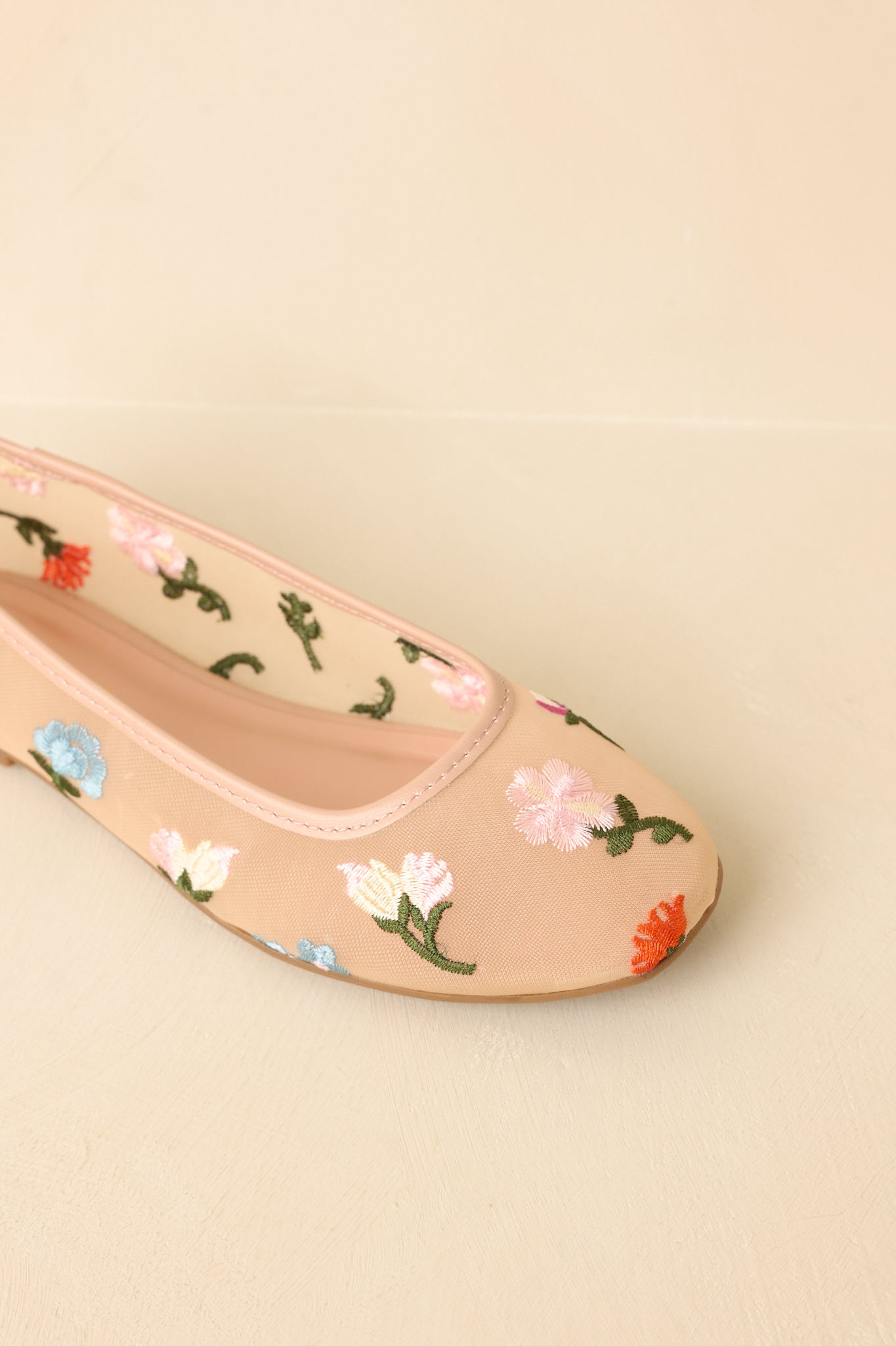 Top-down view of ballet flats on beige background featuring detailed floral embroidery and rounded toe