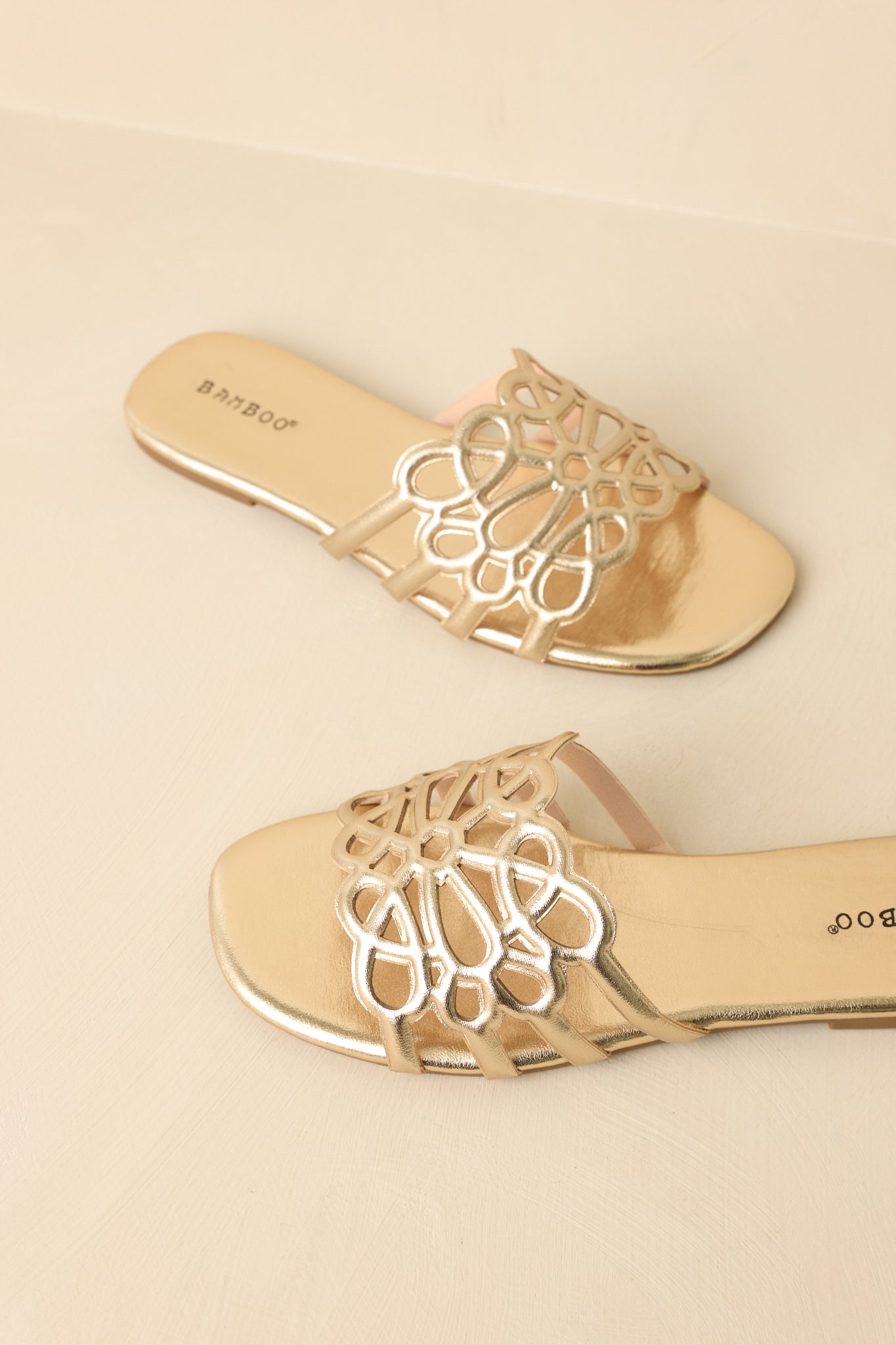Top-down view of gold slide sandals on beige background showing open toe and wide cutout strap