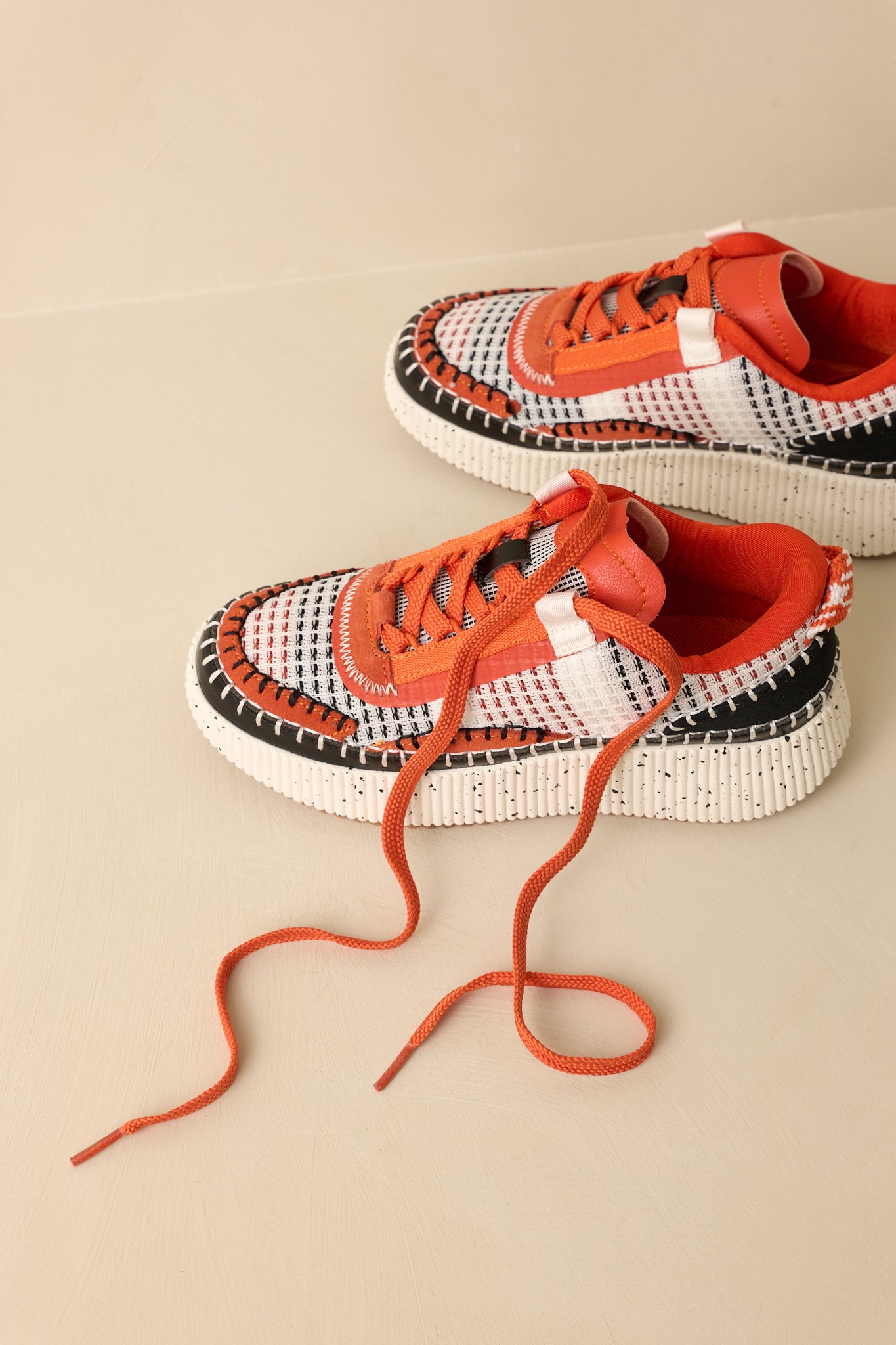 Top-down view of the orange multicolor sneakers against a beige background showcasing the lace placement and woven upper pattern.