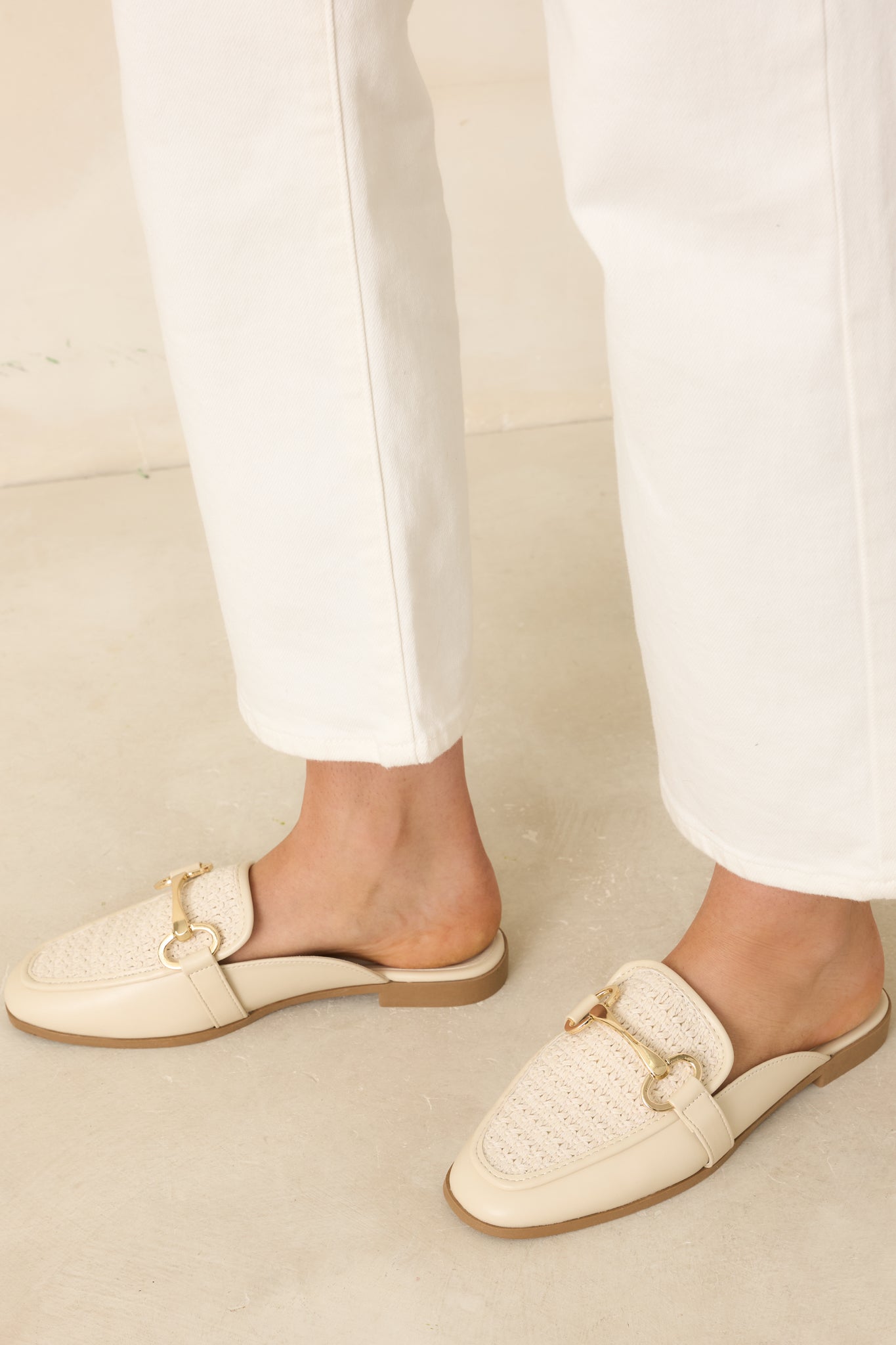 Angled top view of ivory mule loafers against a beige background highlighting the clean silhouette and textured finish.