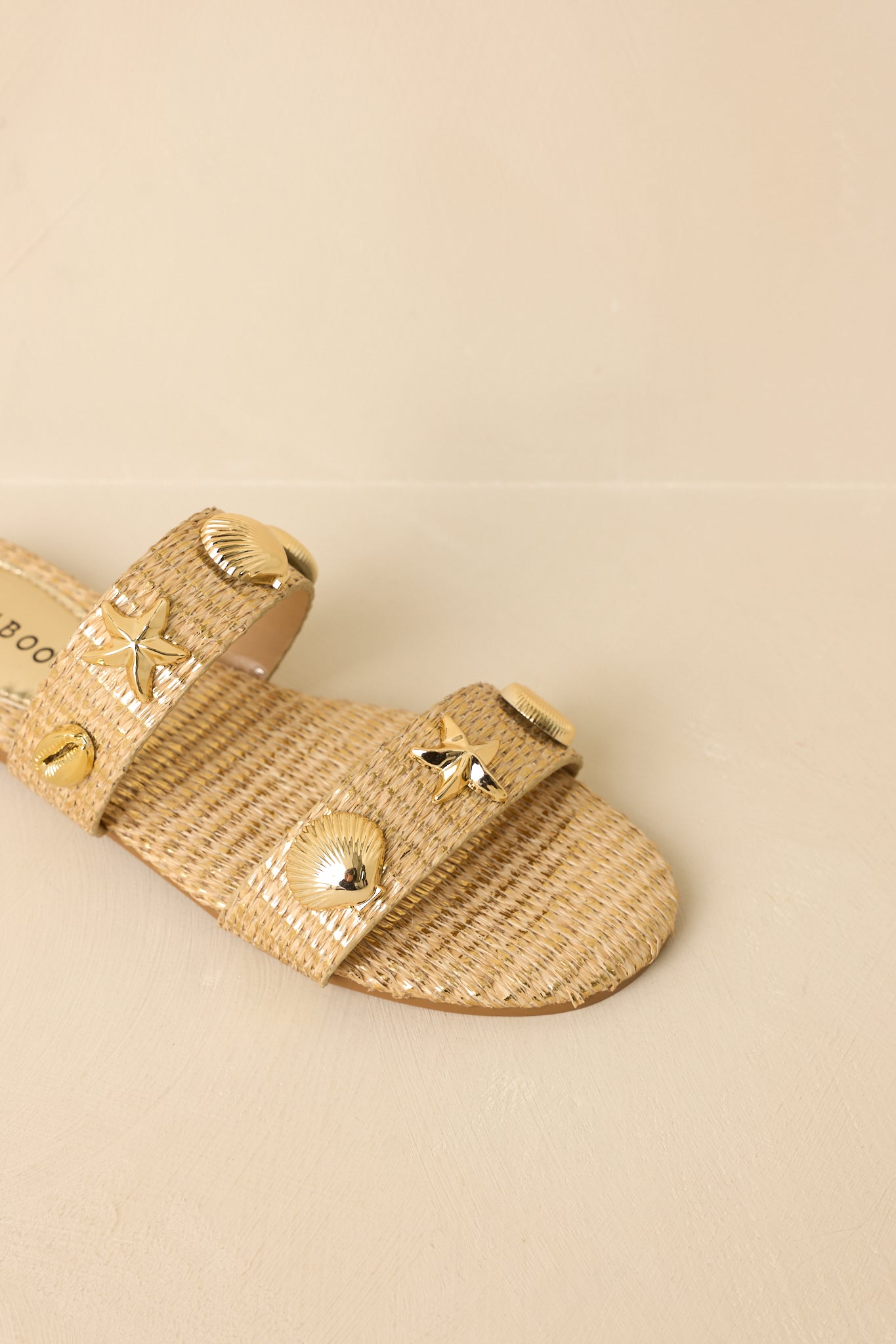 Angled top view of gold raffia sandals against a beige background showcasing the intricate woven design and accents.
