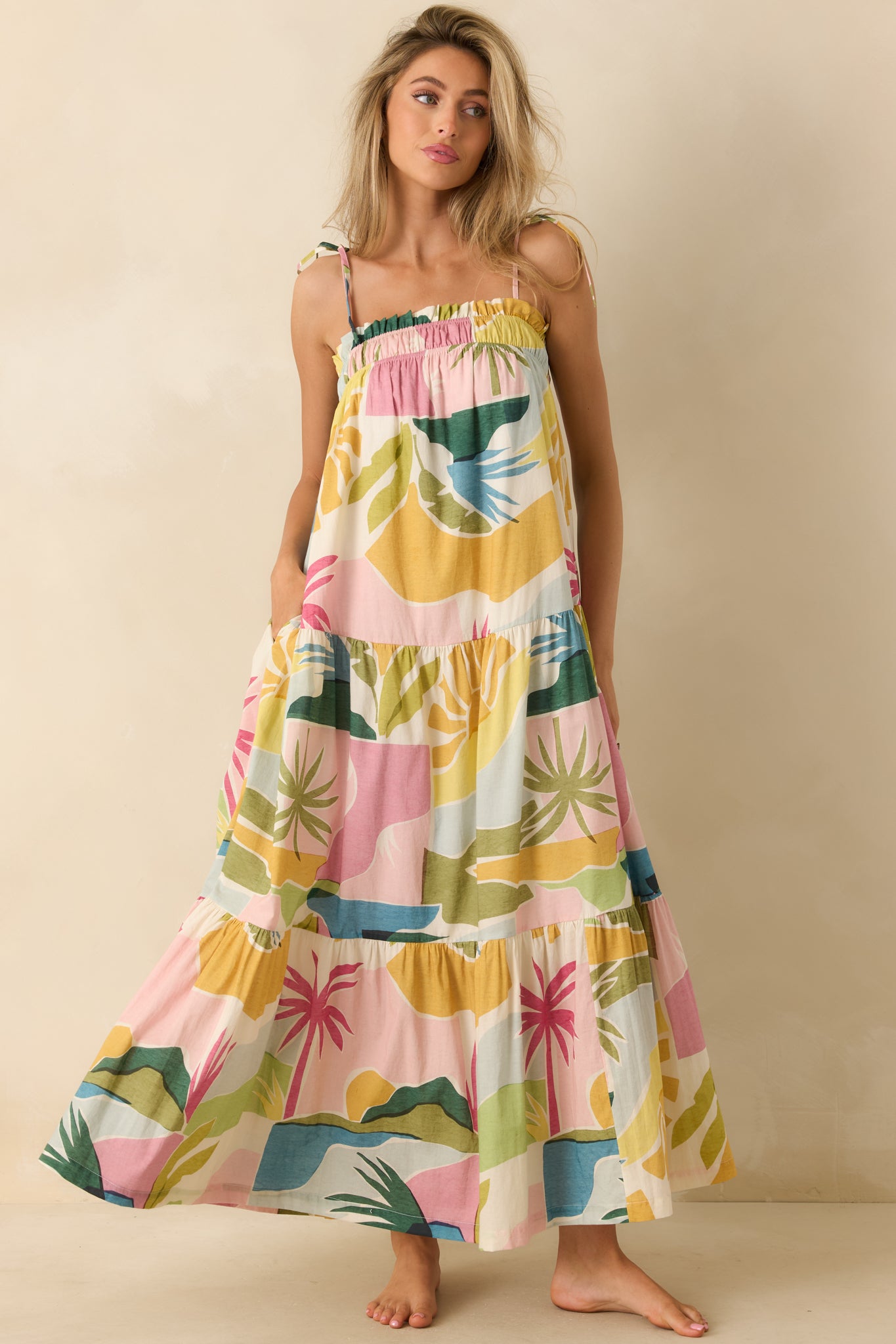 Tropical lagoon print maxi dress featuring a softly gathered neckline, adjustable tie shoulder straps, and a flowing tiered skirt in vibrant pink, green, blue, and golden yellow hues.