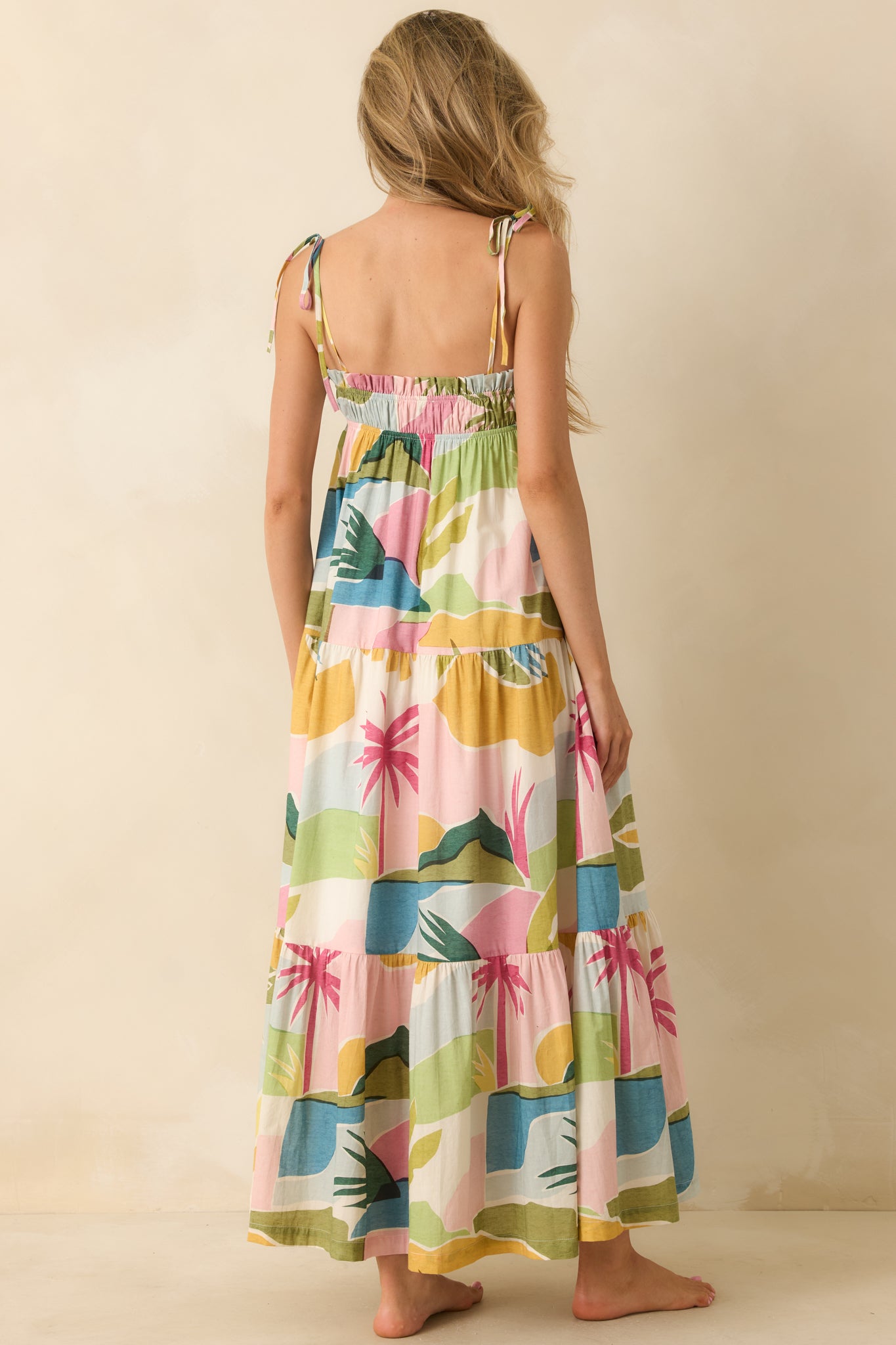 Tropical lagoon print maxi dress highlighting the elasticized back, adjustable tie shoulder straps, and flowing tiered skirt construction.