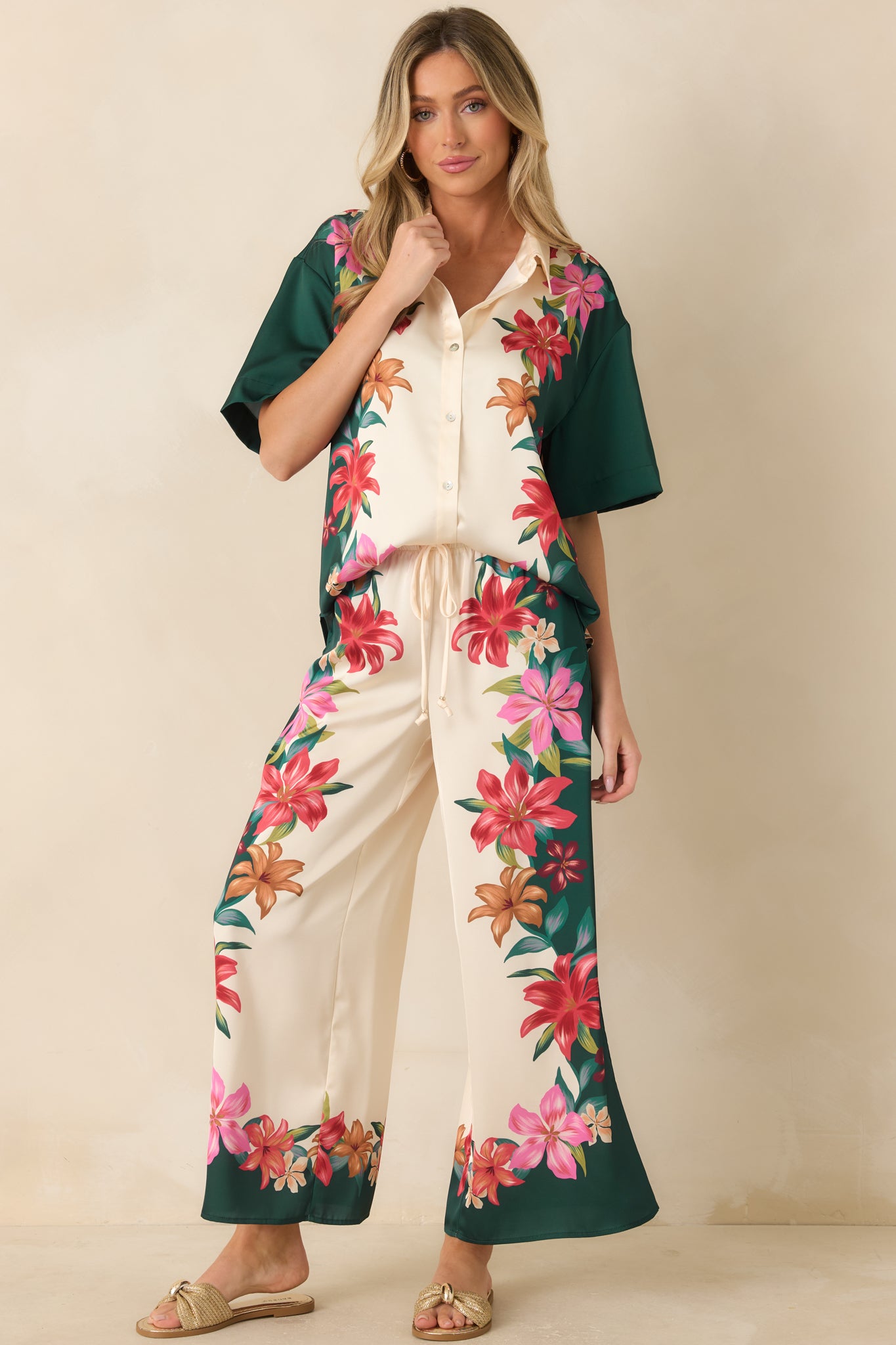 Tropical-inspired teal satin top featuring colorful floral detailing, soft draping fabric, and an effortless short sleeve design.