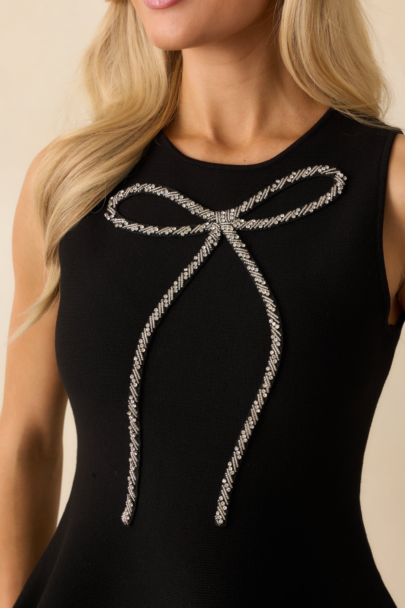 Up-close view of the intricate beaded bow detailing and the smooth knit texture surrounding it.