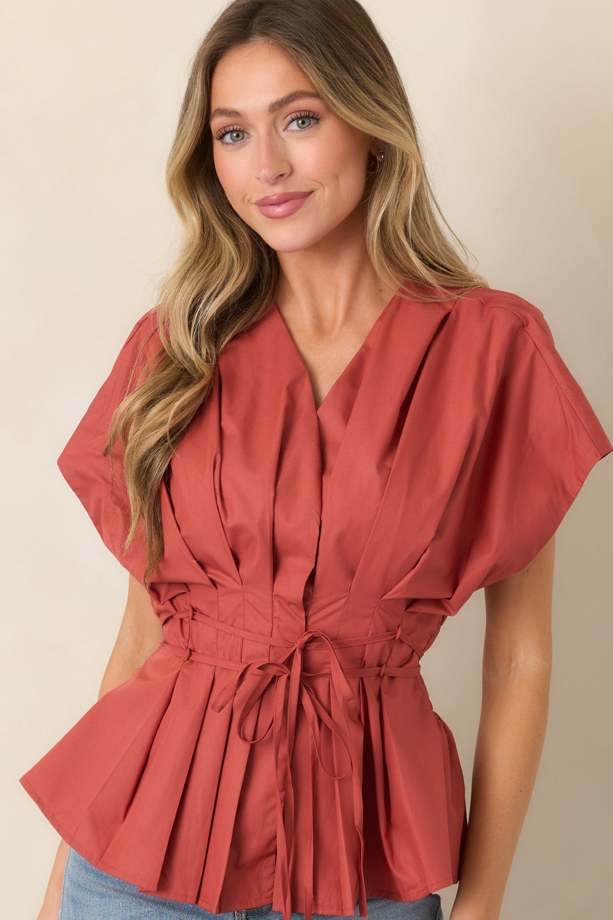 V-neck top highlighting the slender waist ties, intricate pleating, and voluminous short sleeves.