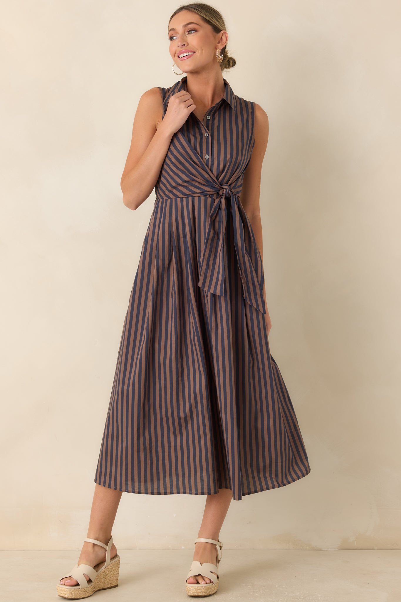 Vertical striped midi dress featuring a sleeveless silhouette, gathered waist detail, and soft flowing skirt shape.