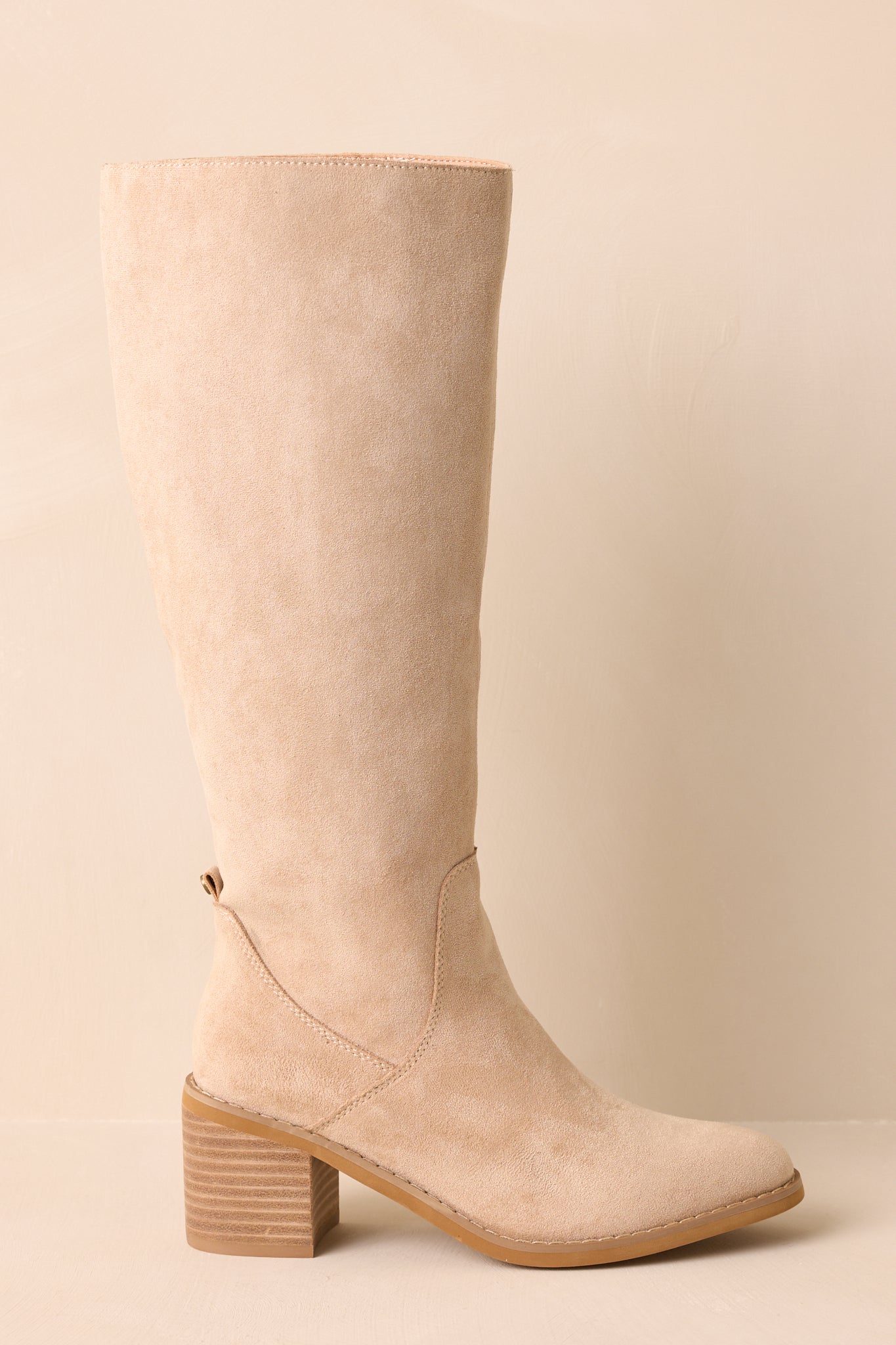 Cropped view of beige knee-high boots with a soft faux suede finish and almond toe.