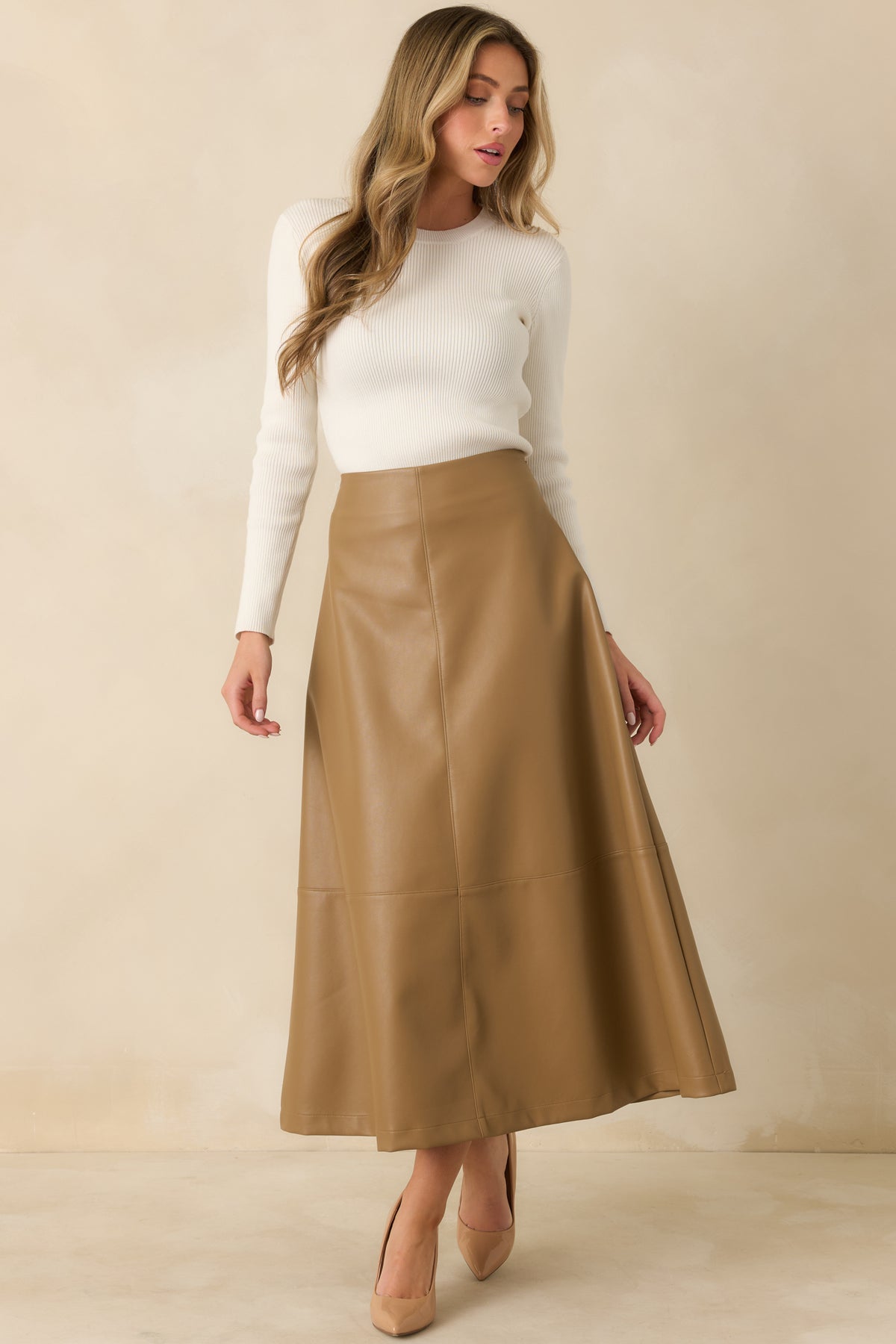 Warm caramel midi skirt showcasing smooth vegan leather, clean panel seams, and a polished flared shape.
