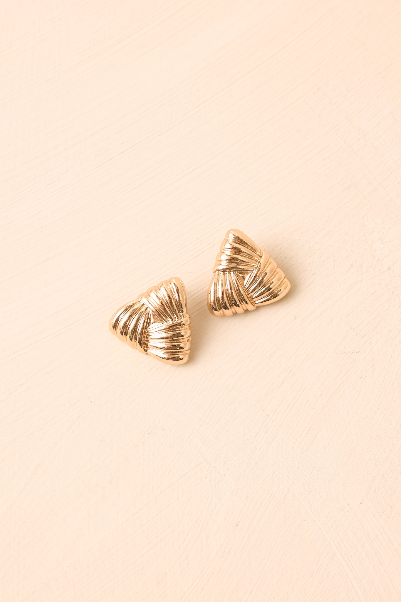 The Weaving Our Story gold stud earrings displayed against a beige background, highlighting their textured pleated construction.