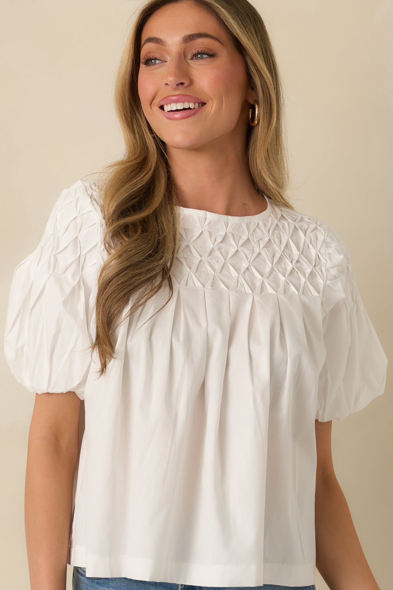 Front cropped angle of a white blouse focusing on the puff sleeves with elastic cuffs and smocked texture.