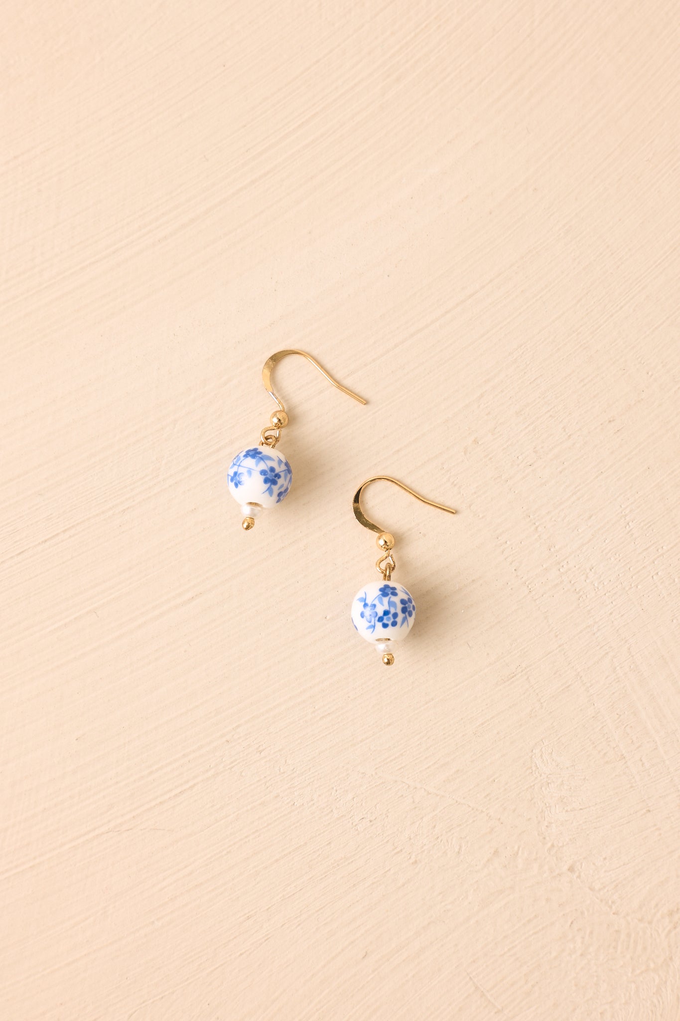 White and blue porcelain-style bead earrings displayed against a beige background with gold-tone accents.