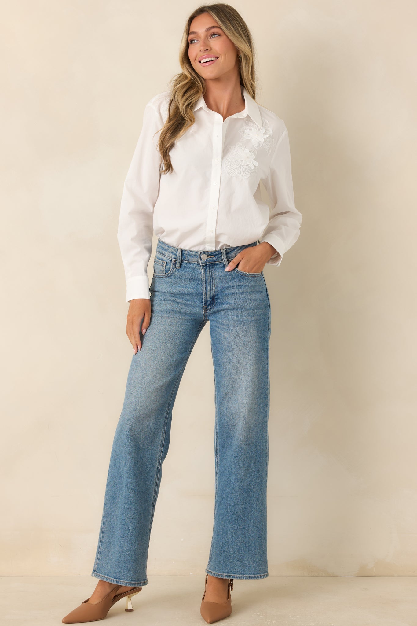 White woven blouse featuring a classic collared neckline, floral appliqué details, long sleeves, and a relaxed button-down silhouette.