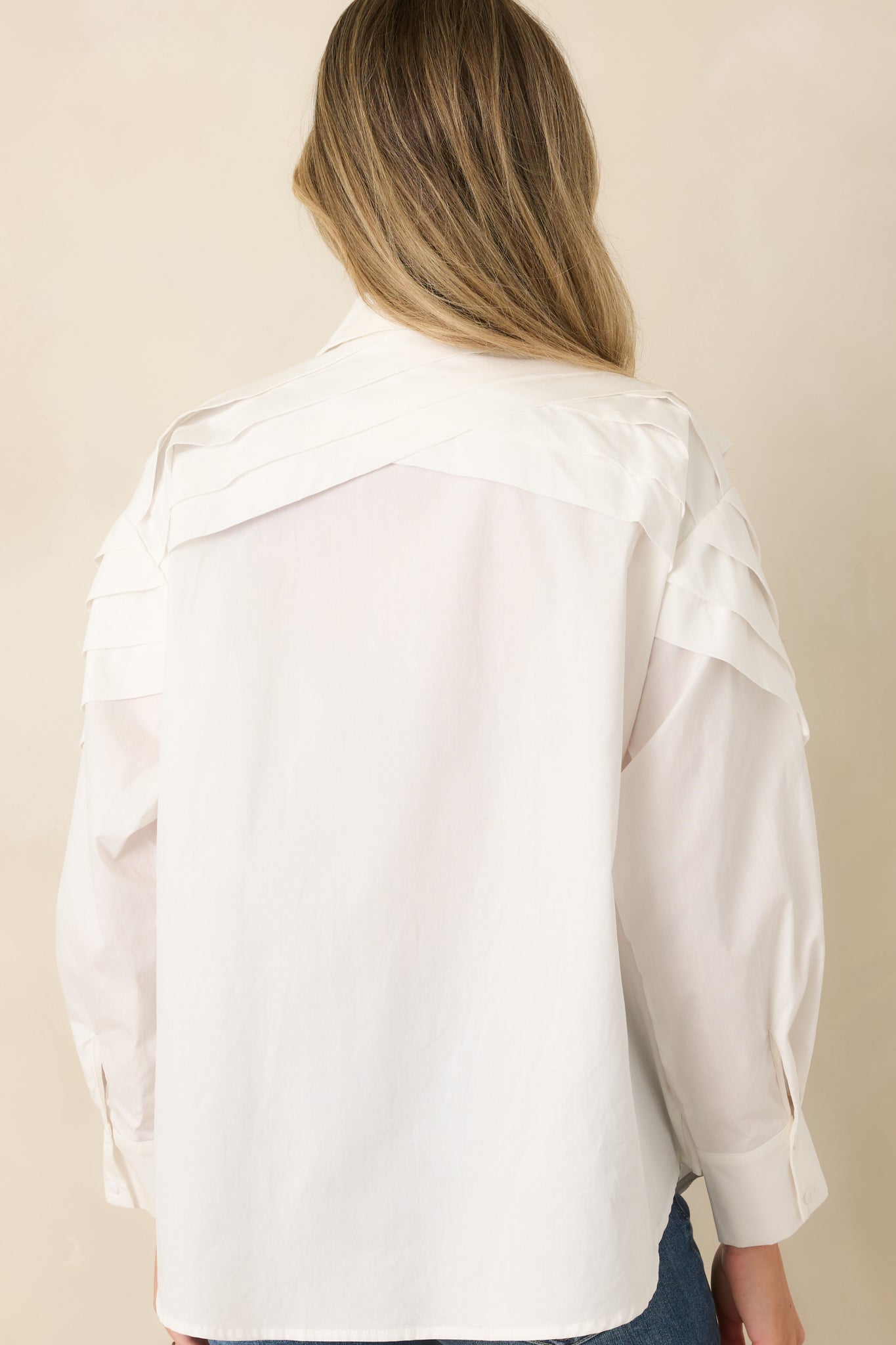 Rear view of the white cotton blouse featuring pleated shoulders and a structured relaxed silhouette.