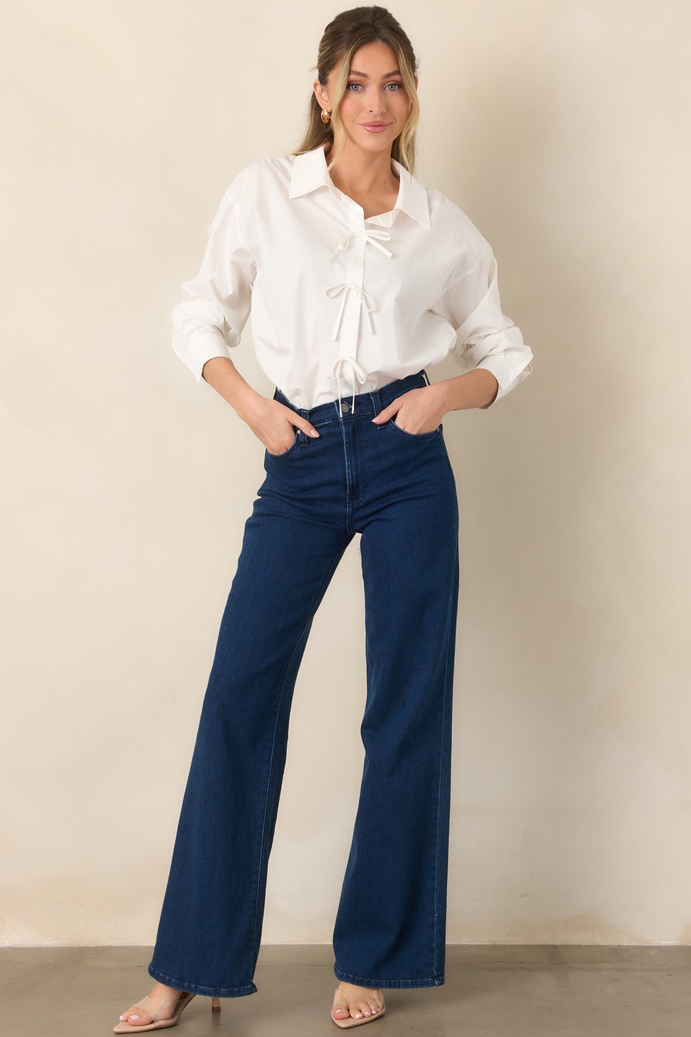White cotton button-front top featuring a collared neckline, long sleeves, relaxed fit, and delicate white bow details between each button.