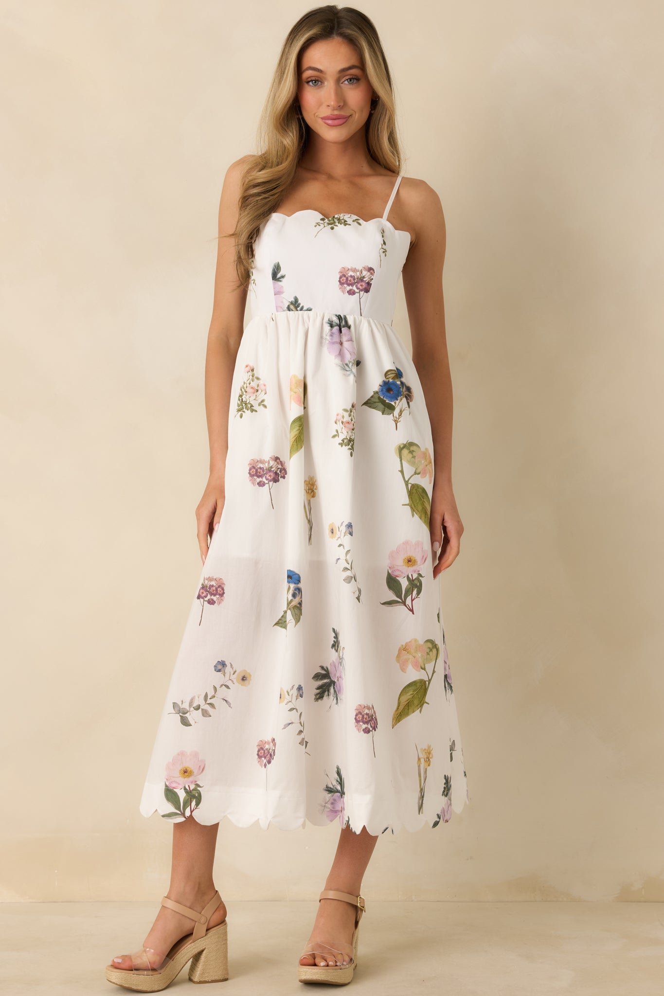 Flowing white cotton dress with scalloped neckline and hem, adjustable straps, and fitted bodice with tie-back accent.