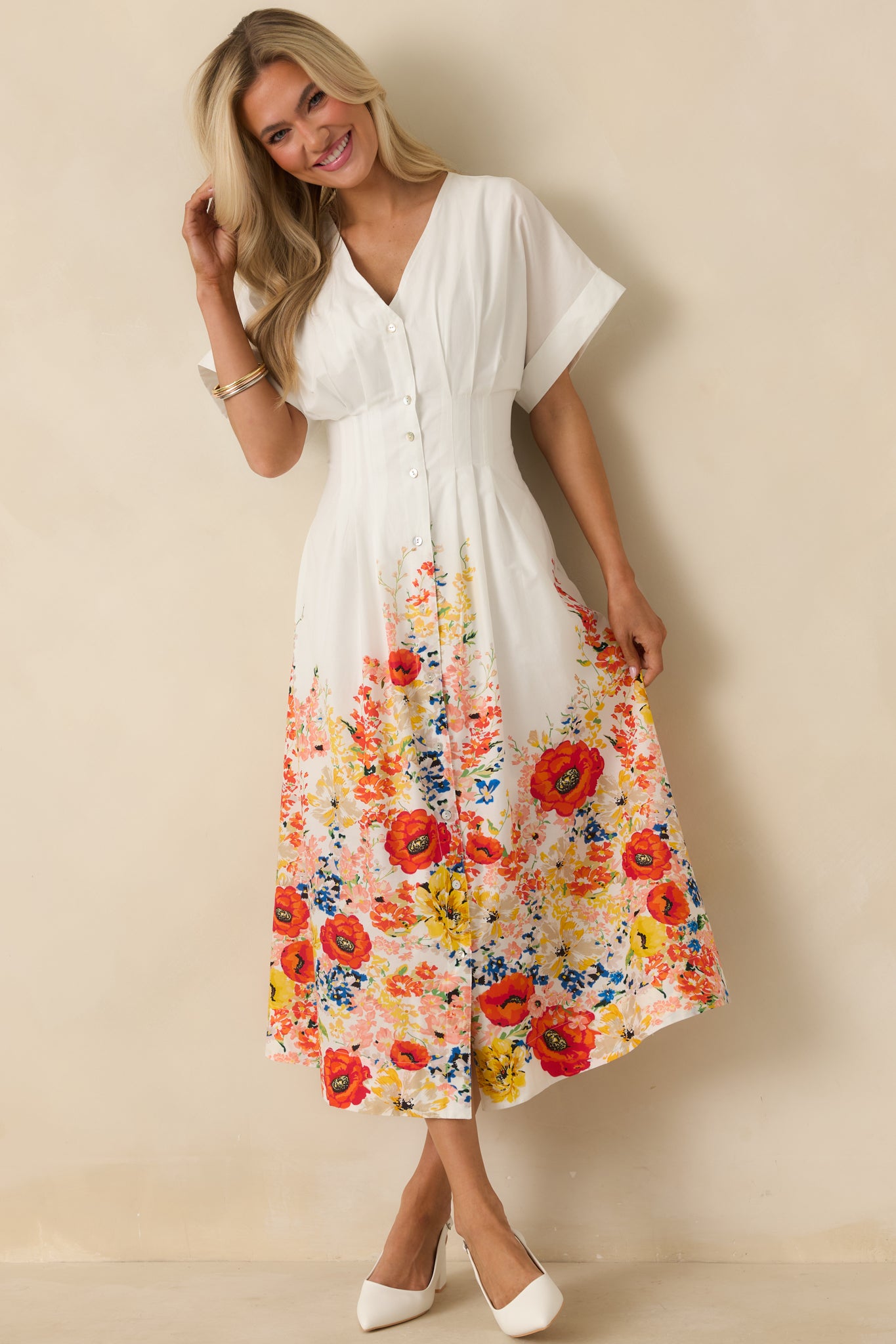 White cotton midi dress featuring a relaxed flowy skirt, defined waist seam, V-neckline, flutter sleeves, and a colorful floral border along the hem.