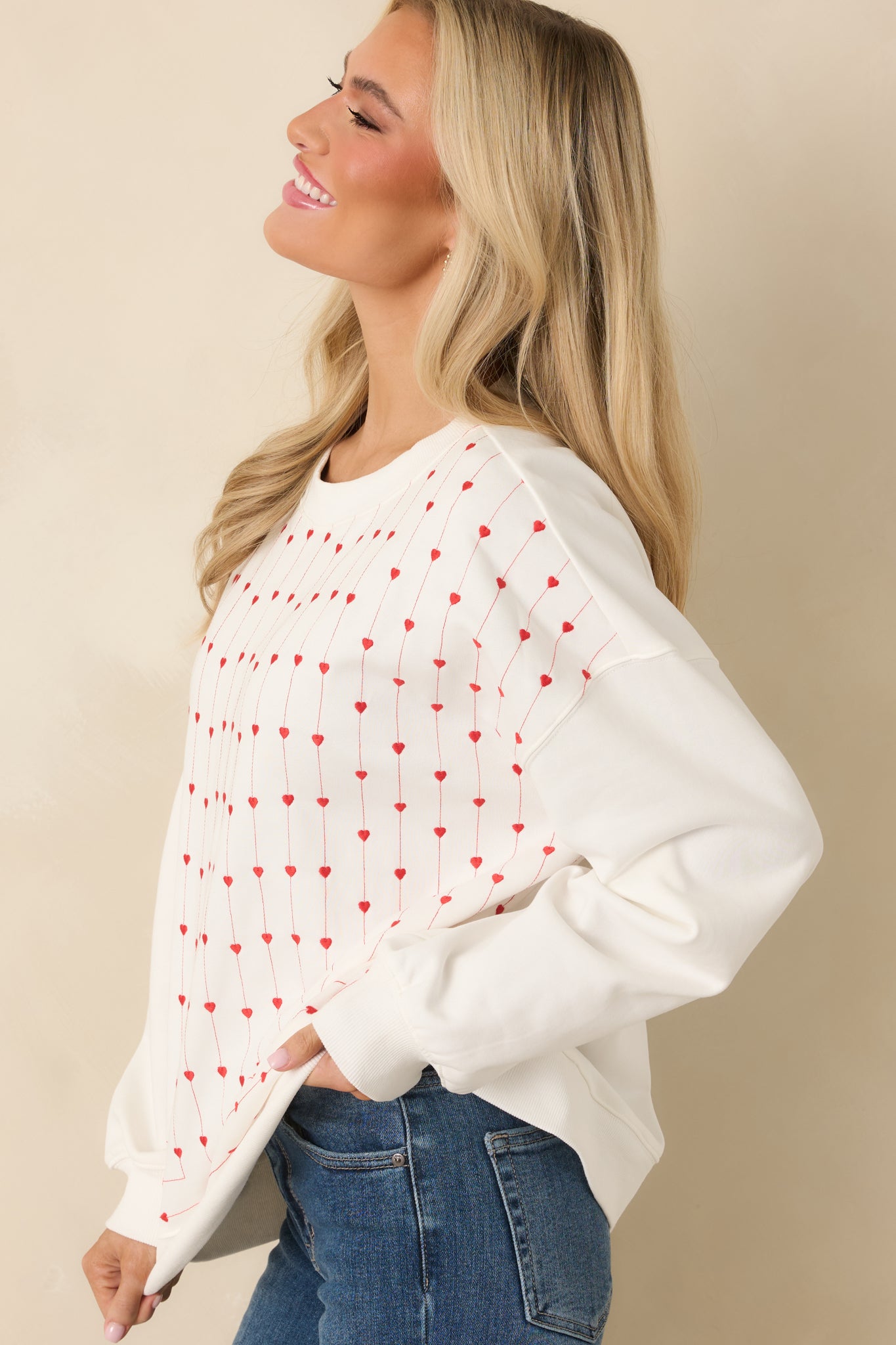 Bright white cotton sweatshirt featuring slim vertical lines of embroidered hearts along the front, with ribbed cuff and hem accents for structure.