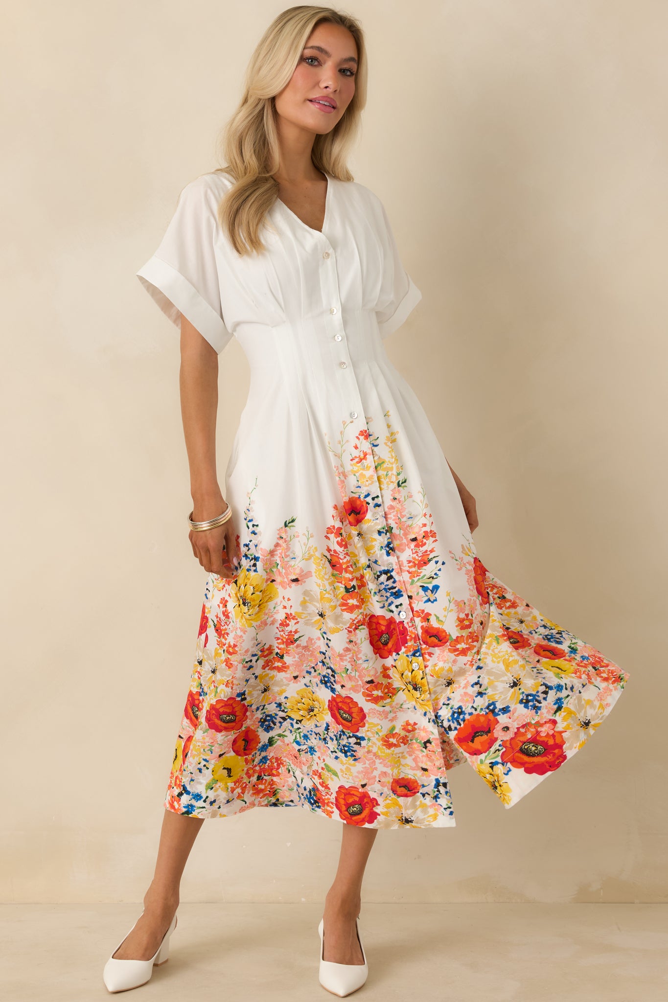 Flowy white midi dress showcasing a shaped waist seam, functional buttons, and a multicolor floral print along the hem.