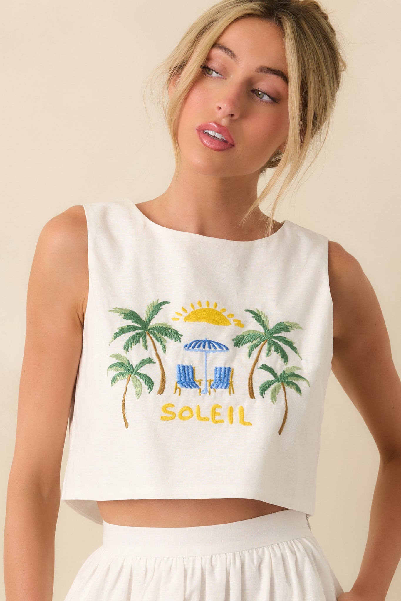 White embroidered top close-up showing sun motif and textured stitching.