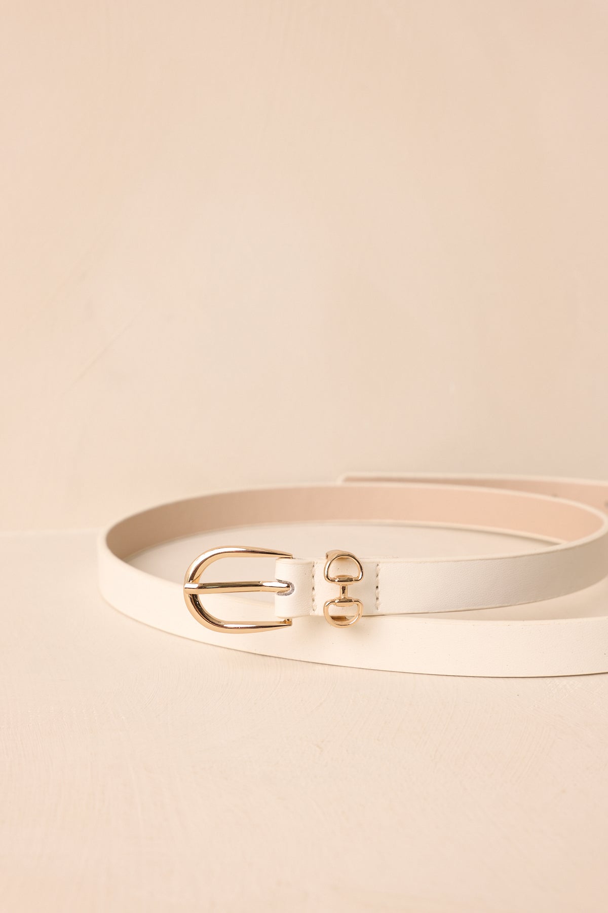 Close-up highlights the gold-tone double ring buckle, smooth white faux leather, and punched adjustment holes.