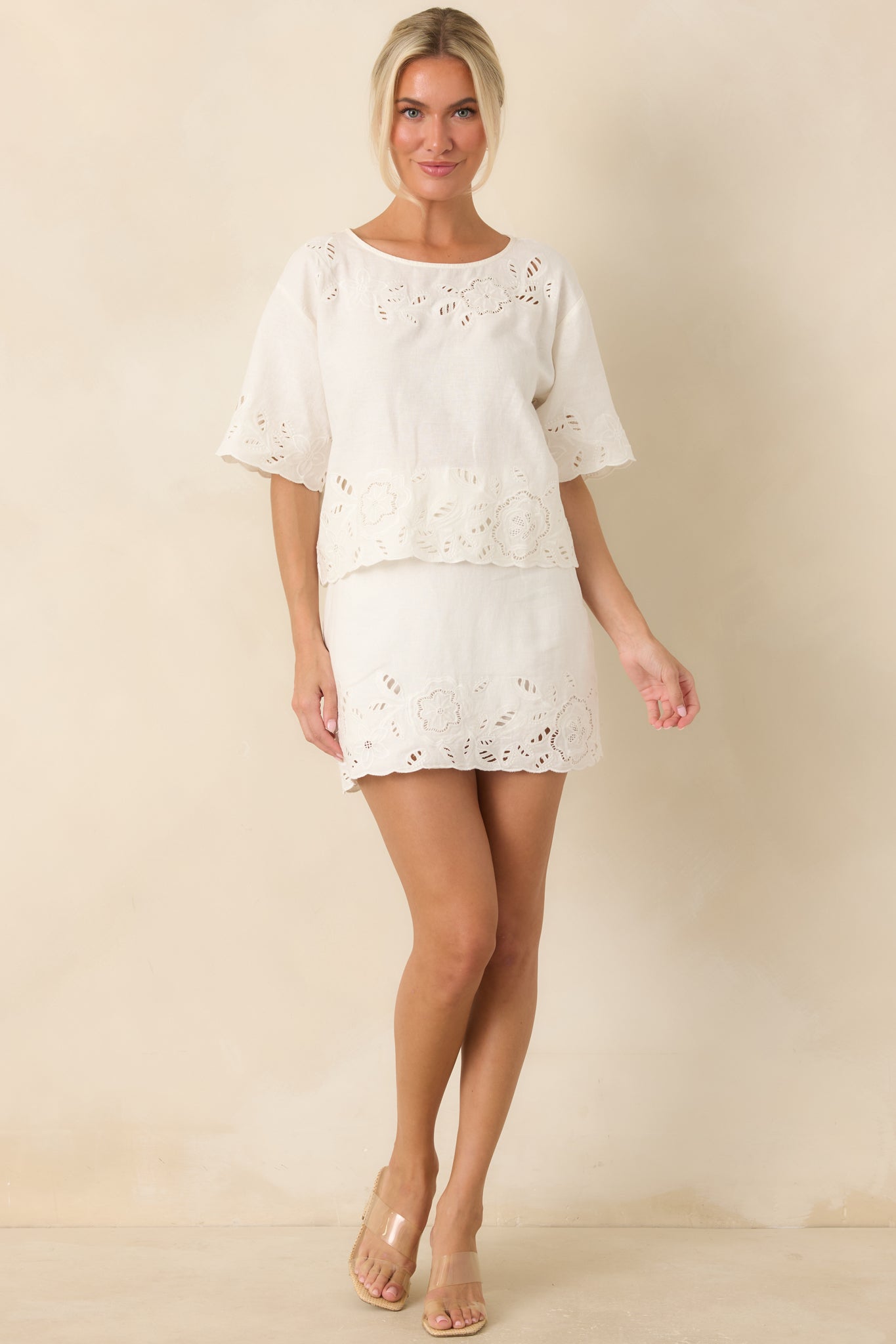 White linen-blend top featuring floral cutwork embroidery, a classic round neckline, short sleeves, and a relaxed silhouette.