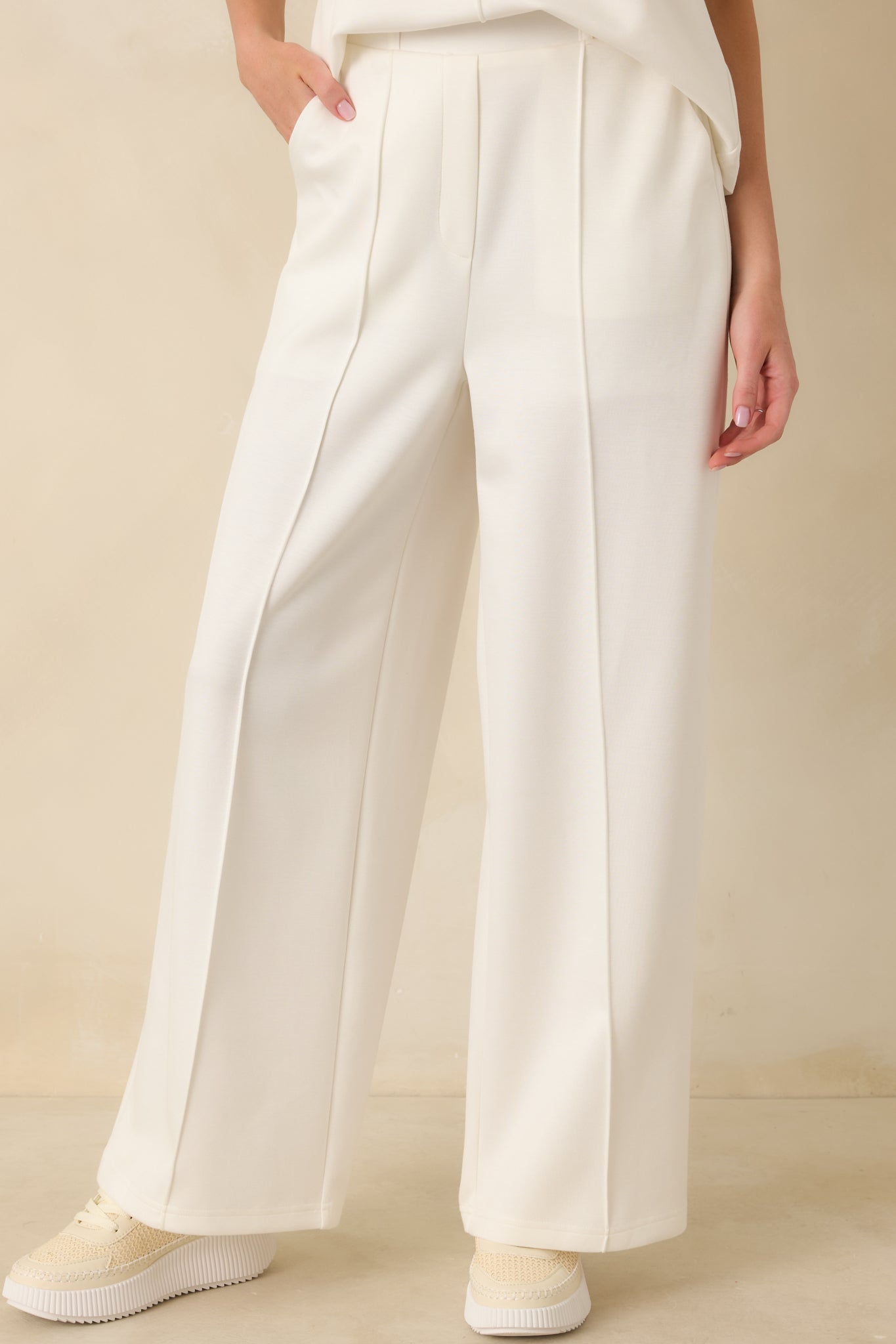 White high-waisted pants emphasizing the front pleats and clean hem finish.
