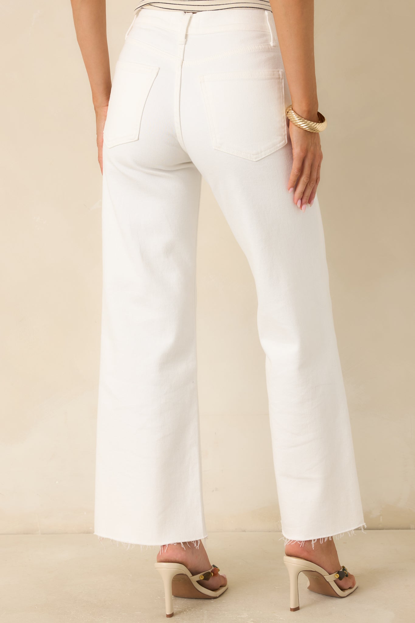 Back view of the white jeans featuring functional back pockets, wide straight legs, and raw hems.