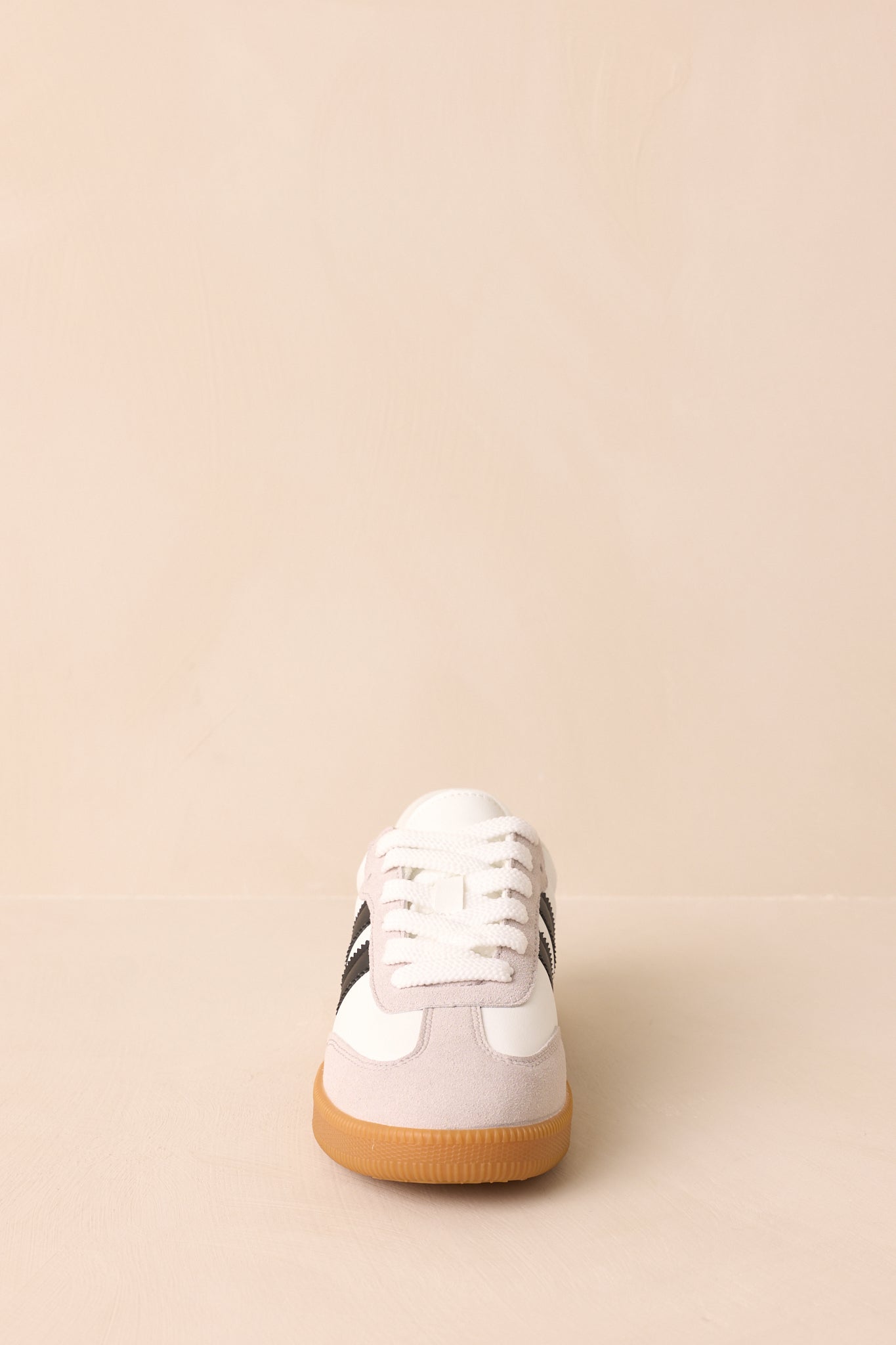 White low-top sneakers with black side stripes and rounded toe, shown from a front angle.