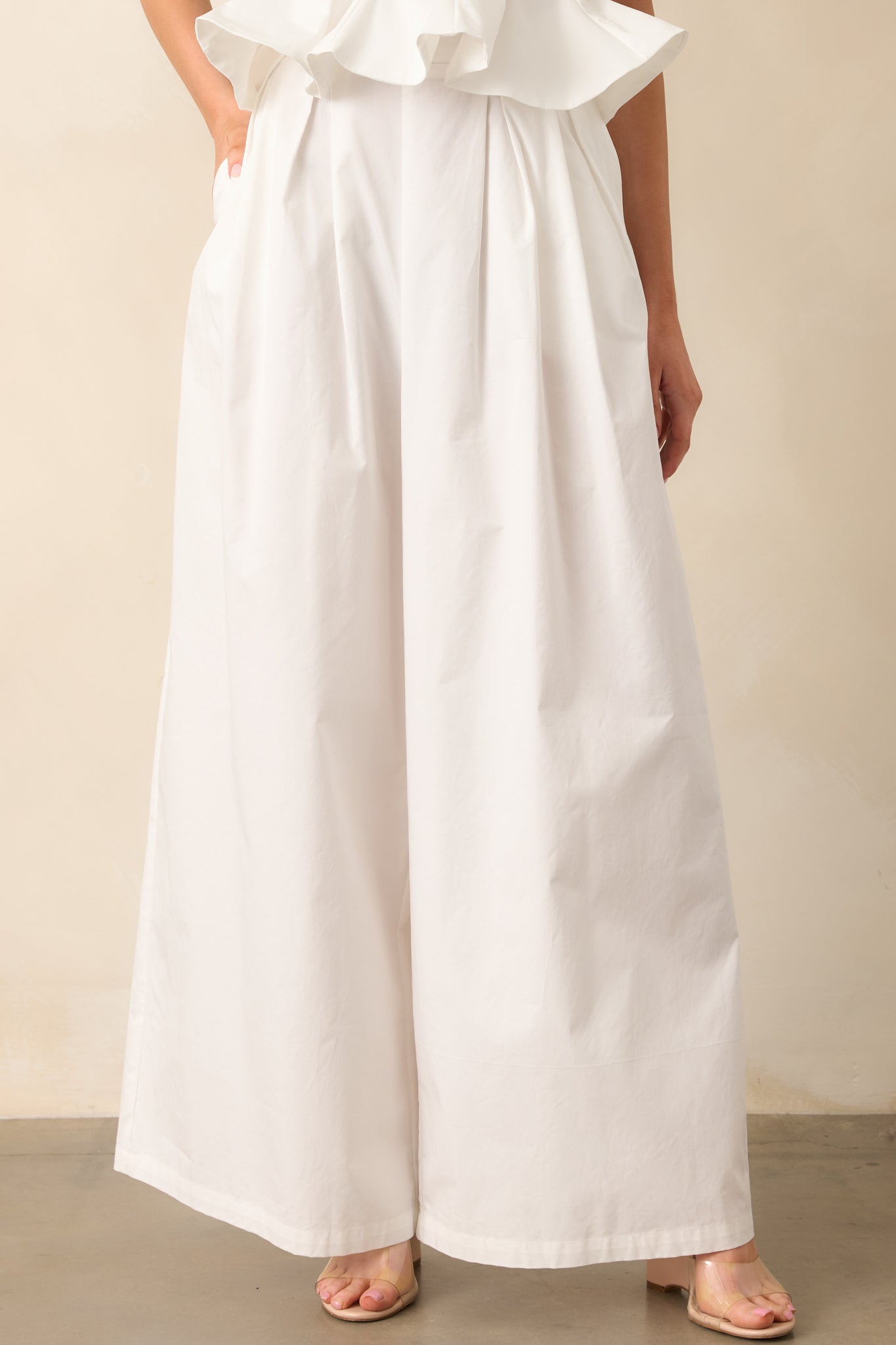 Cropped front view of high-waisted white pants highlighting structured waistband and functional pockets.