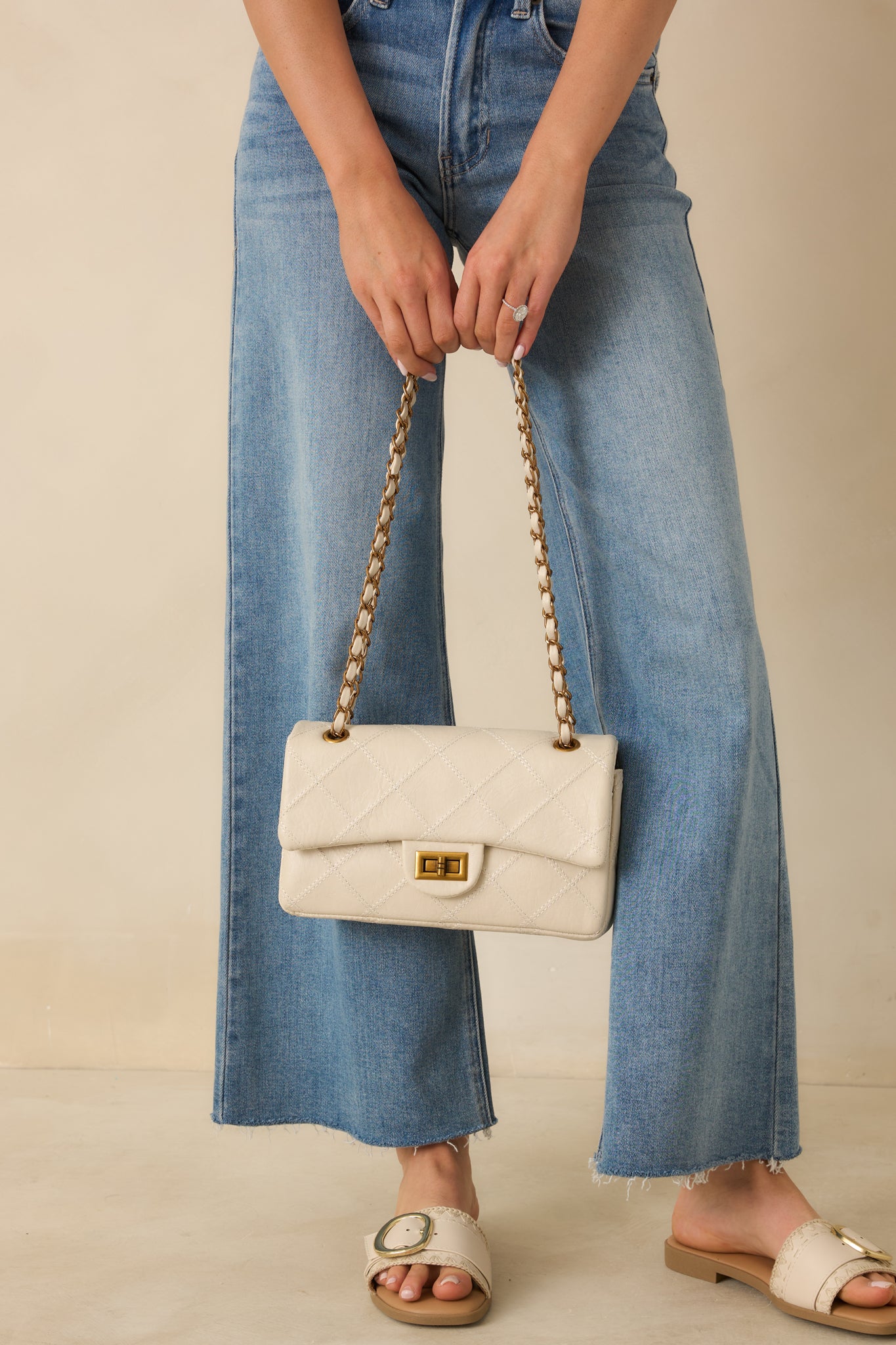 Front view of a white quilted faux leather handbag with a structured silhouette, gold-tone turn-lock closure, and chain strap woven with faux leather.
