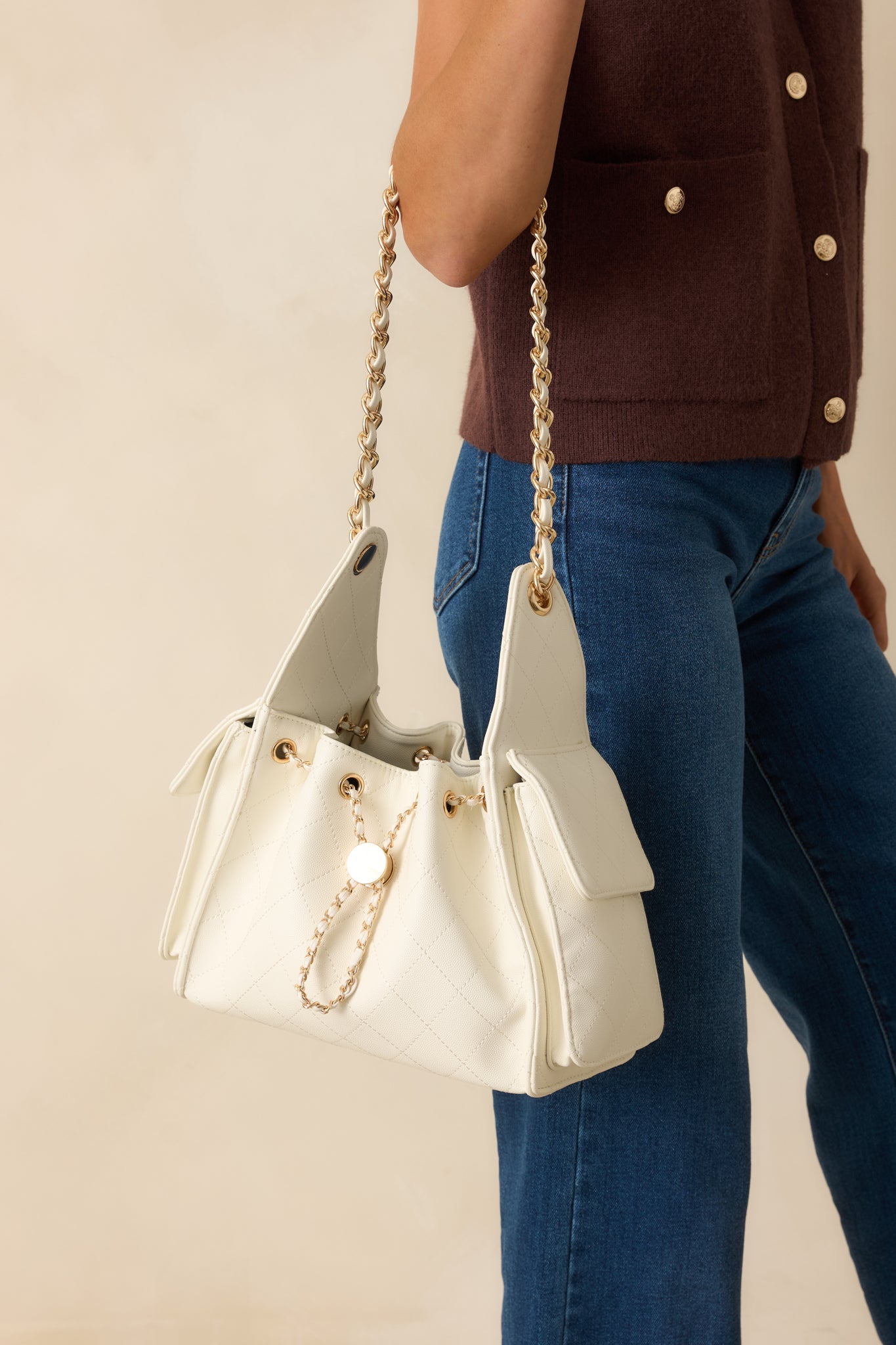 Front view of white quilted purse featuring detachable strap made of faux leather cord interlaced with gold chain and side flap pockets.