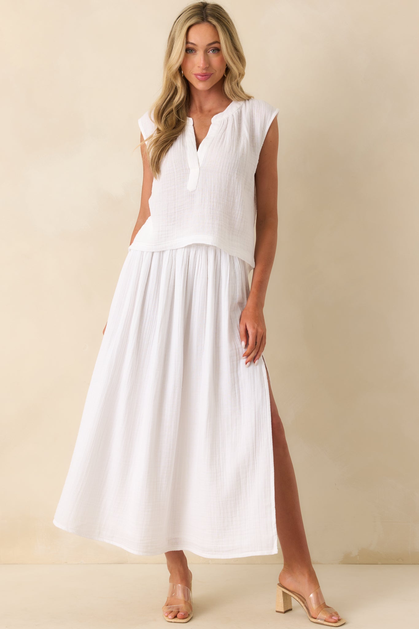 Photo of model wearing a white skirt that features a lightweight 100% cotton gauze fabric, high rise design, elastic waistband, relaxed fit, midi length, leg slit, and wearing a matching top.