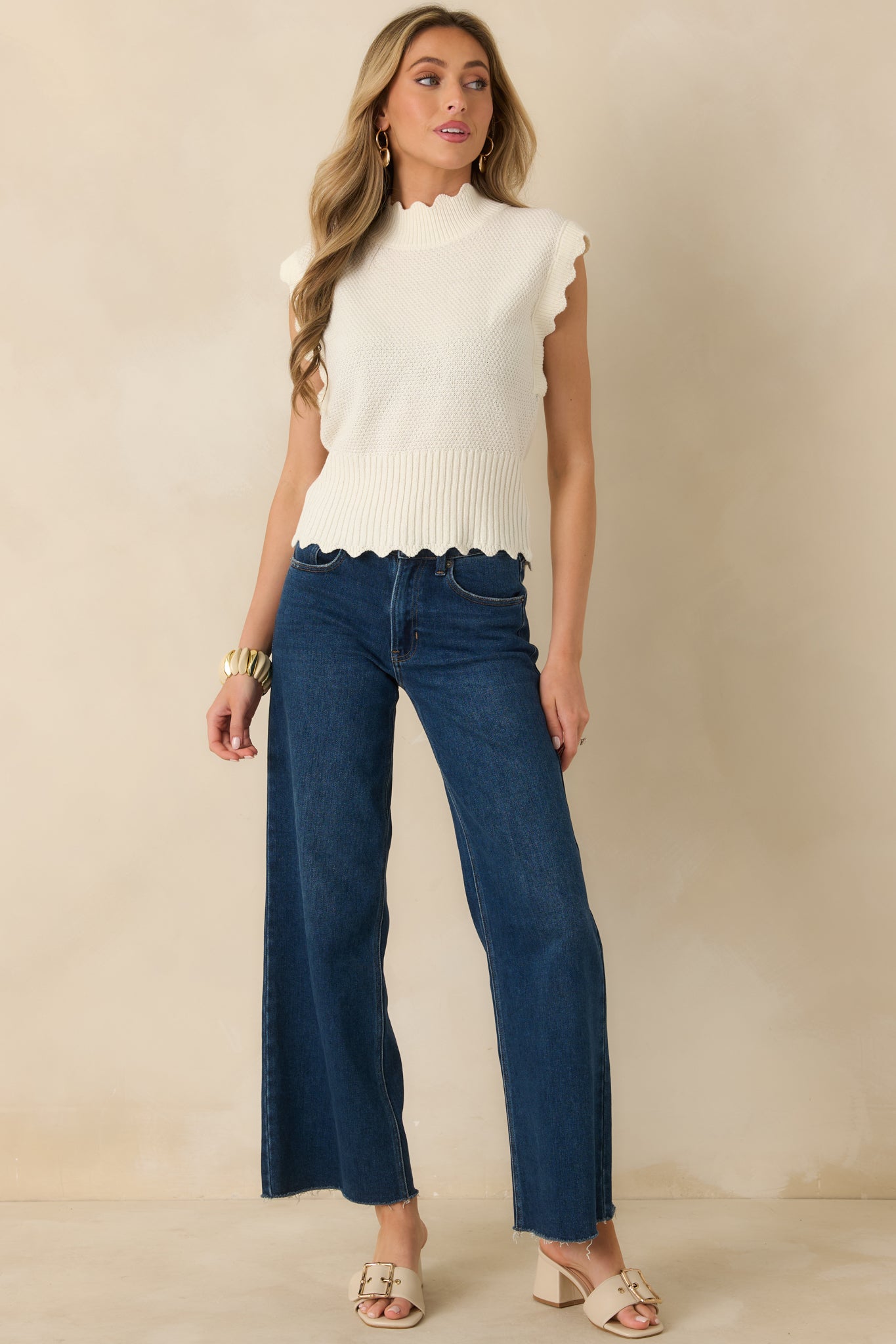White sleeveless sweater with textured knit body, ribbed mock neckline, and wide ribbed hem.