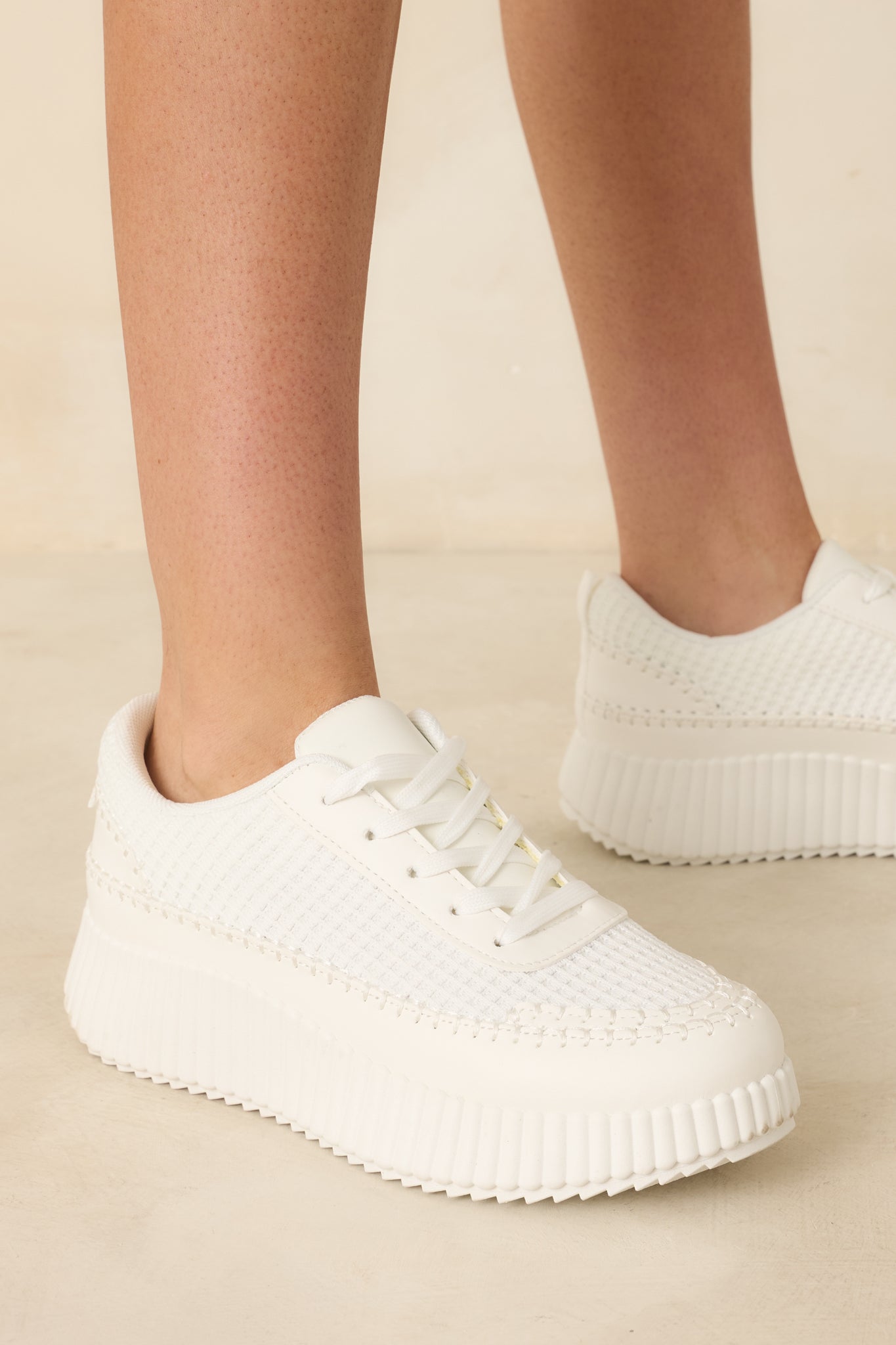 White sneakers with a textured knit upper and lace-up closure, paired with a chunky ribbed platform sole.