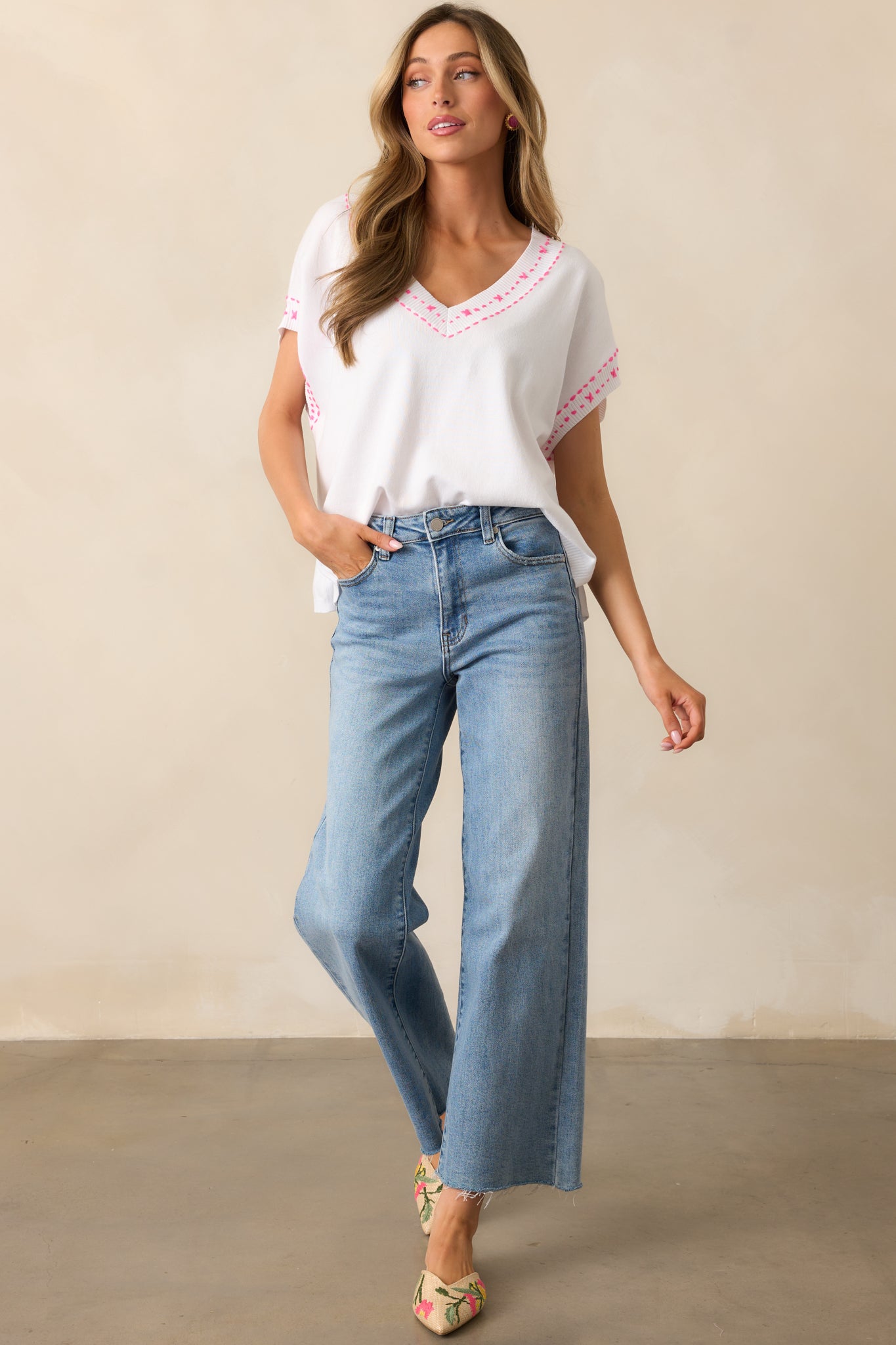 White V-neck top with embroidered pink stitching, wide batwing sleeves, and a draped silhouette, highlighting its effortless style.