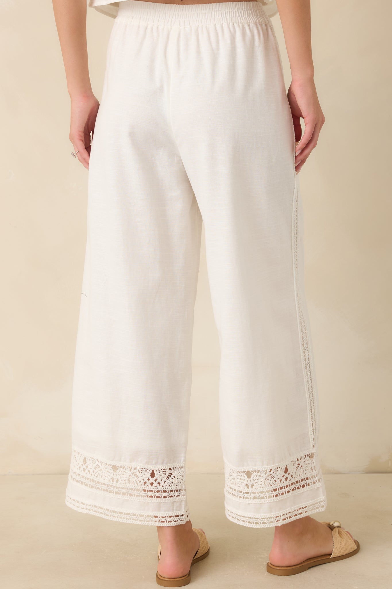 Back view of the white pants featuring a wide-leg cut, elastic waistband, ankle-length hems, and continuous lace trim detailing.