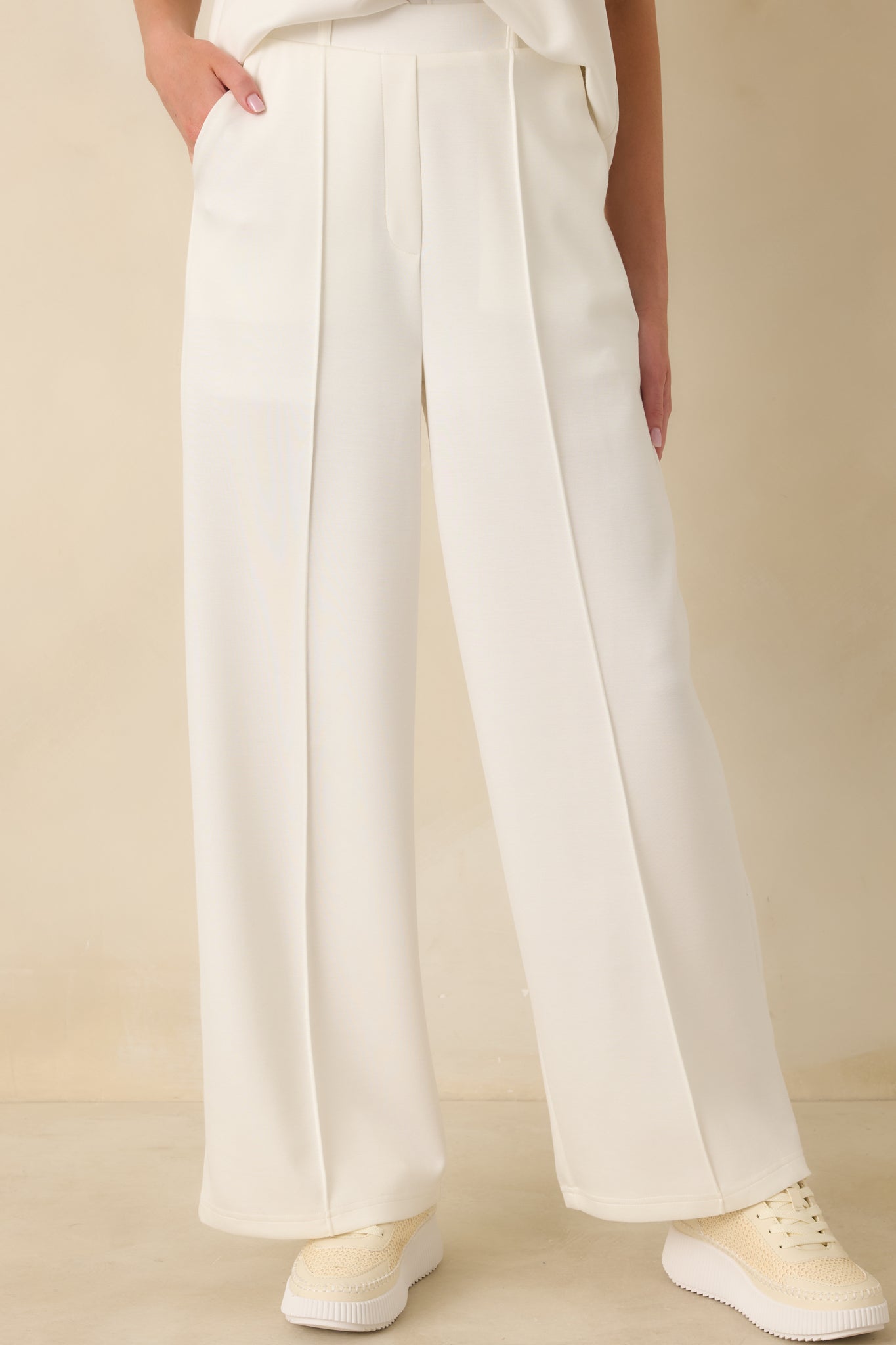 White wide-leg pants highlighting the structured waistband with belt loops and refined pleat detailing.