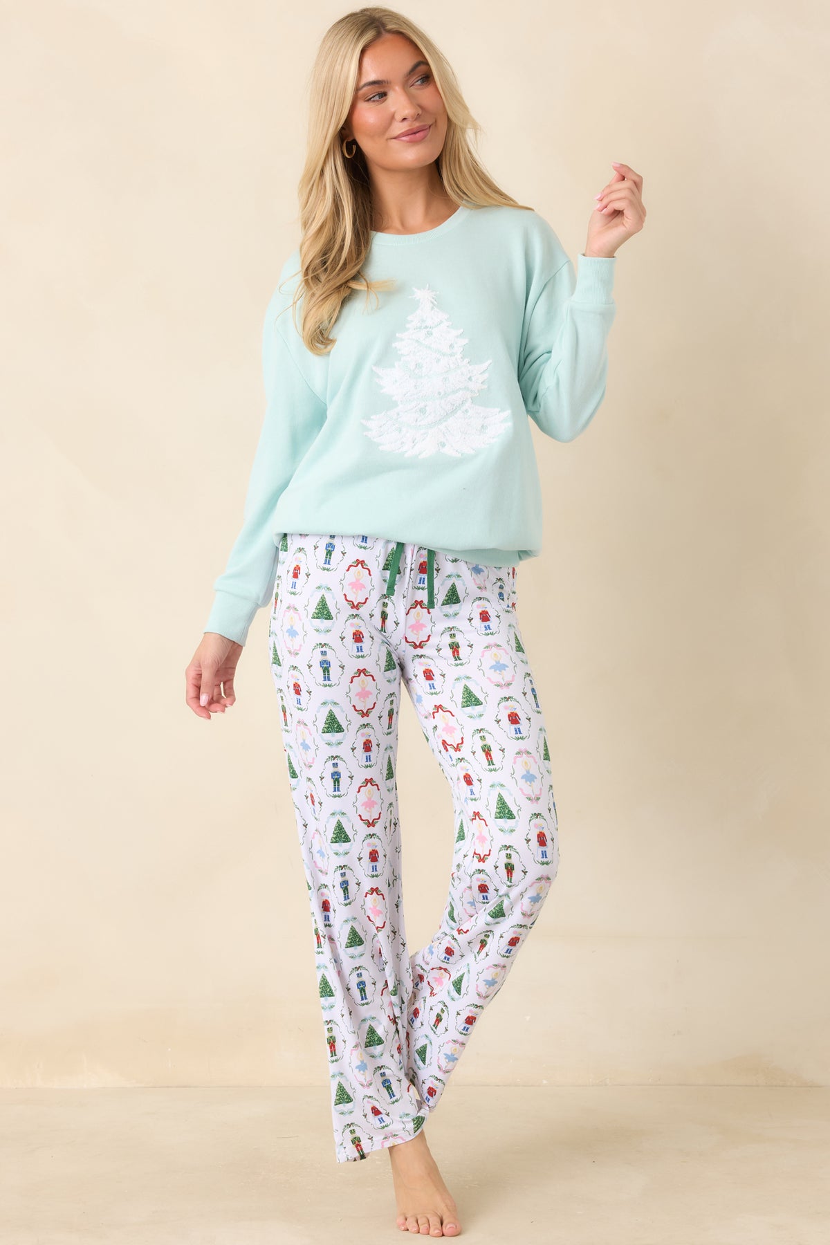 White woven pajama pants feature festive printed motifs, a drawstring waist, and green piping details.