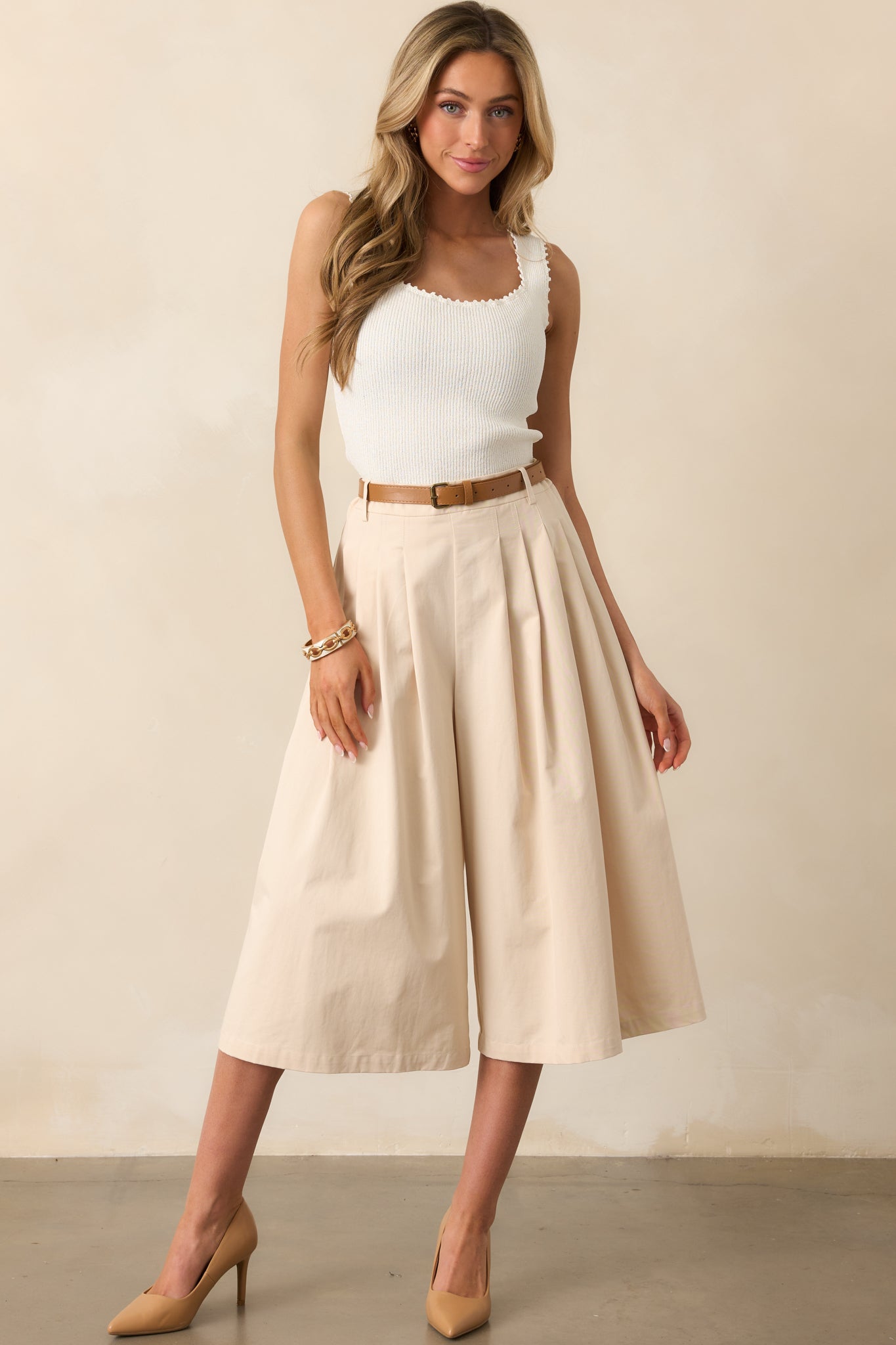 Extra-wide beige pants with a flowing silhouette, cinched at the waist with a cognac brown faux leather belt.