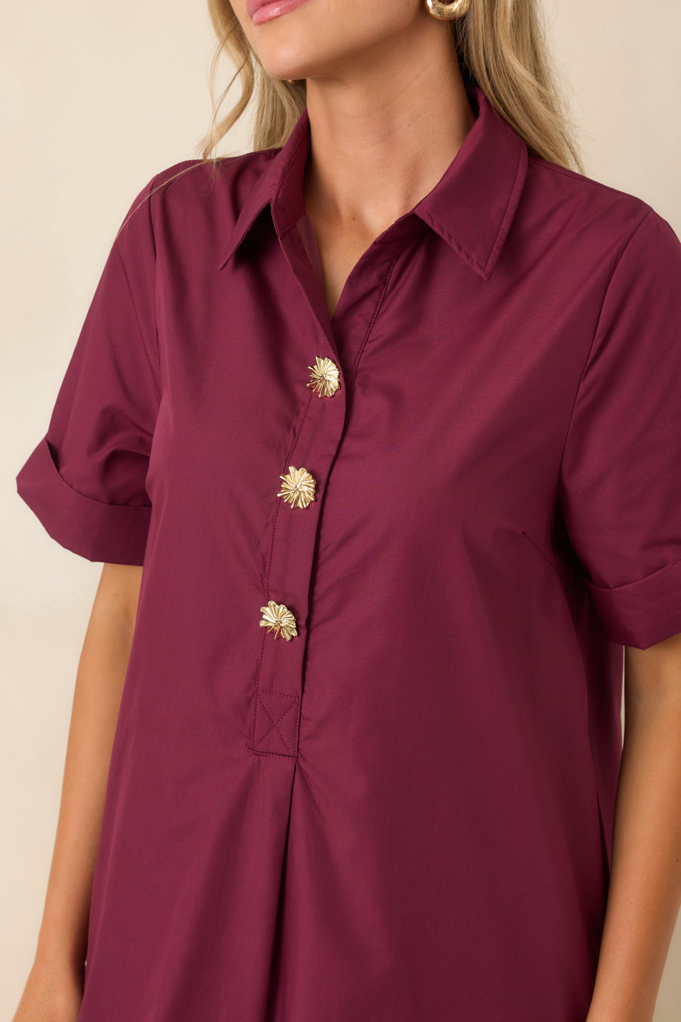 Close-up view of the wine red dress highlighting the gold floral buttons, collar, and woven texture.